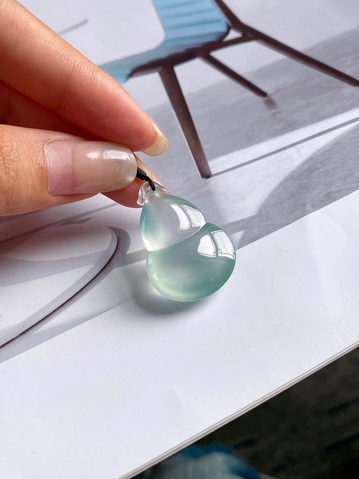 Jadeite gourd pendant held in hand, translucent light-green stone on black cord