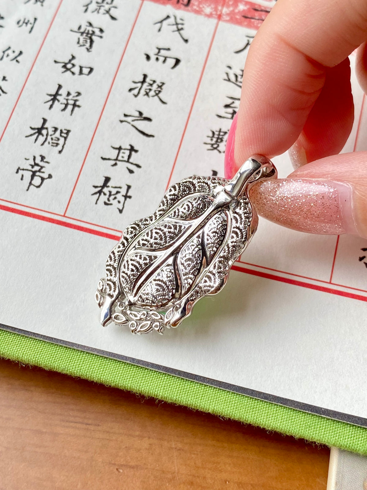 Silver-tone filigree leaf pendant with ornate engraving and green oval setting