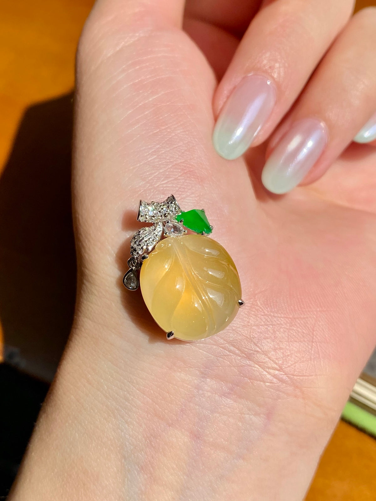 Jadeite leaf pendant on hand: yellow oval cabochon with green leaf accent, clear stones