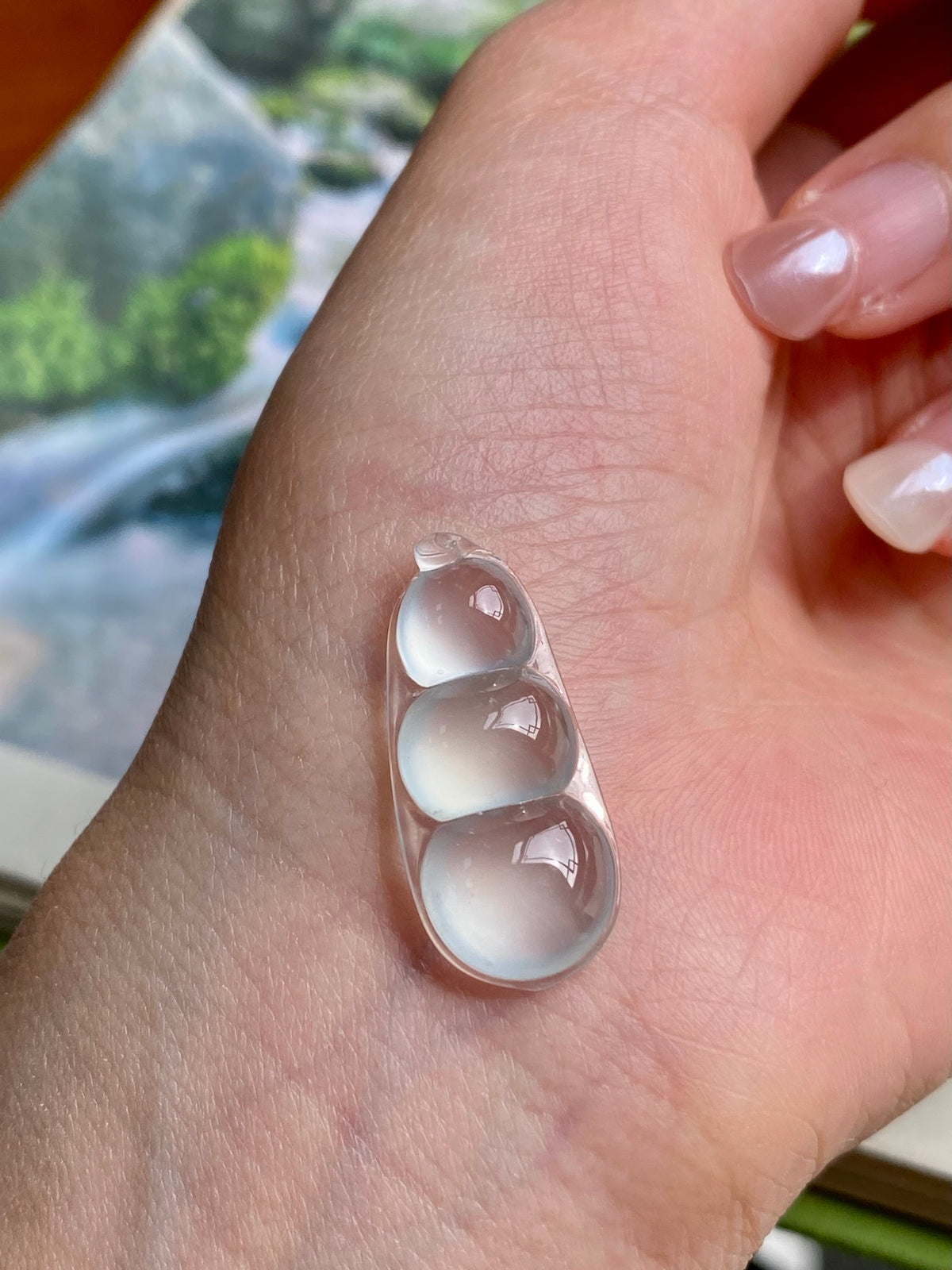 Jadeite bean pendant shown on palm, three milky white oval beads in silver frame