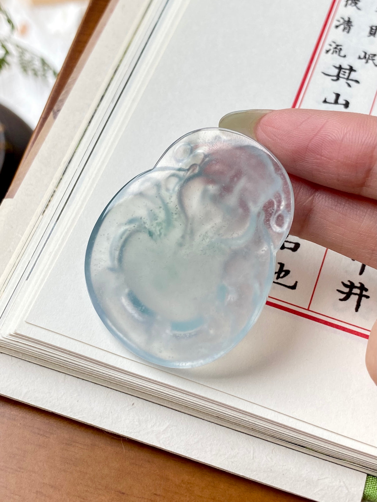 Oval jadeite money god pendant with carved relief, glossy icy white and pale blue-green