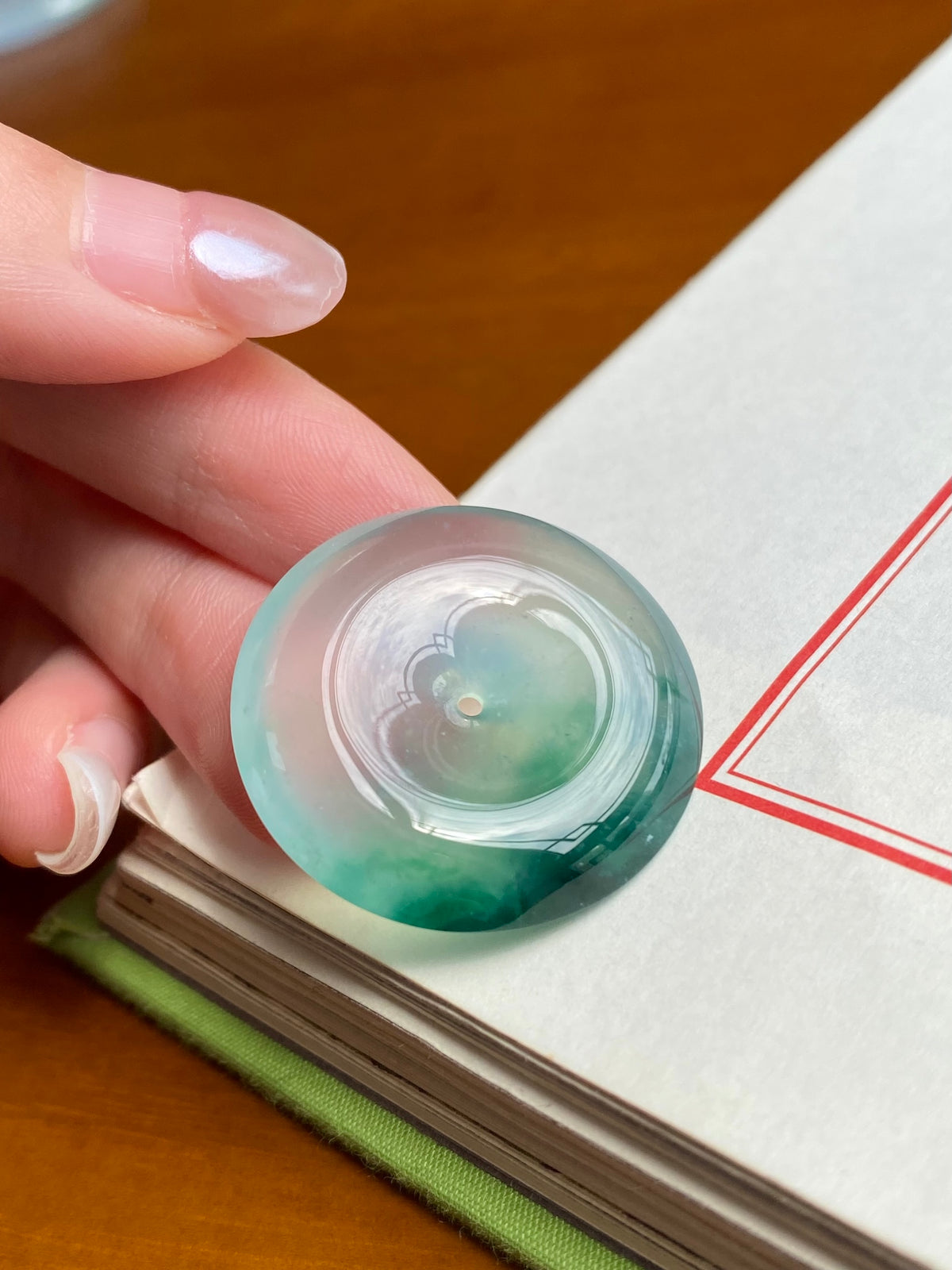 Round green jadeite pendant, clear bezel and reflective center detail, held by fingers