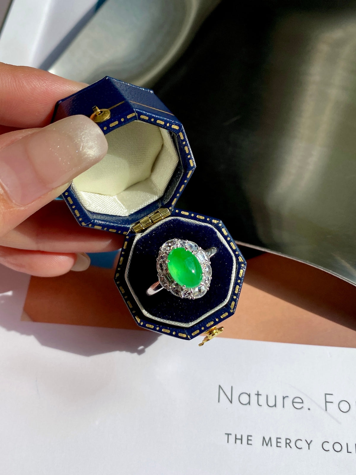 Green jade cabochon ring in blue ring box with silver-tone halo and band