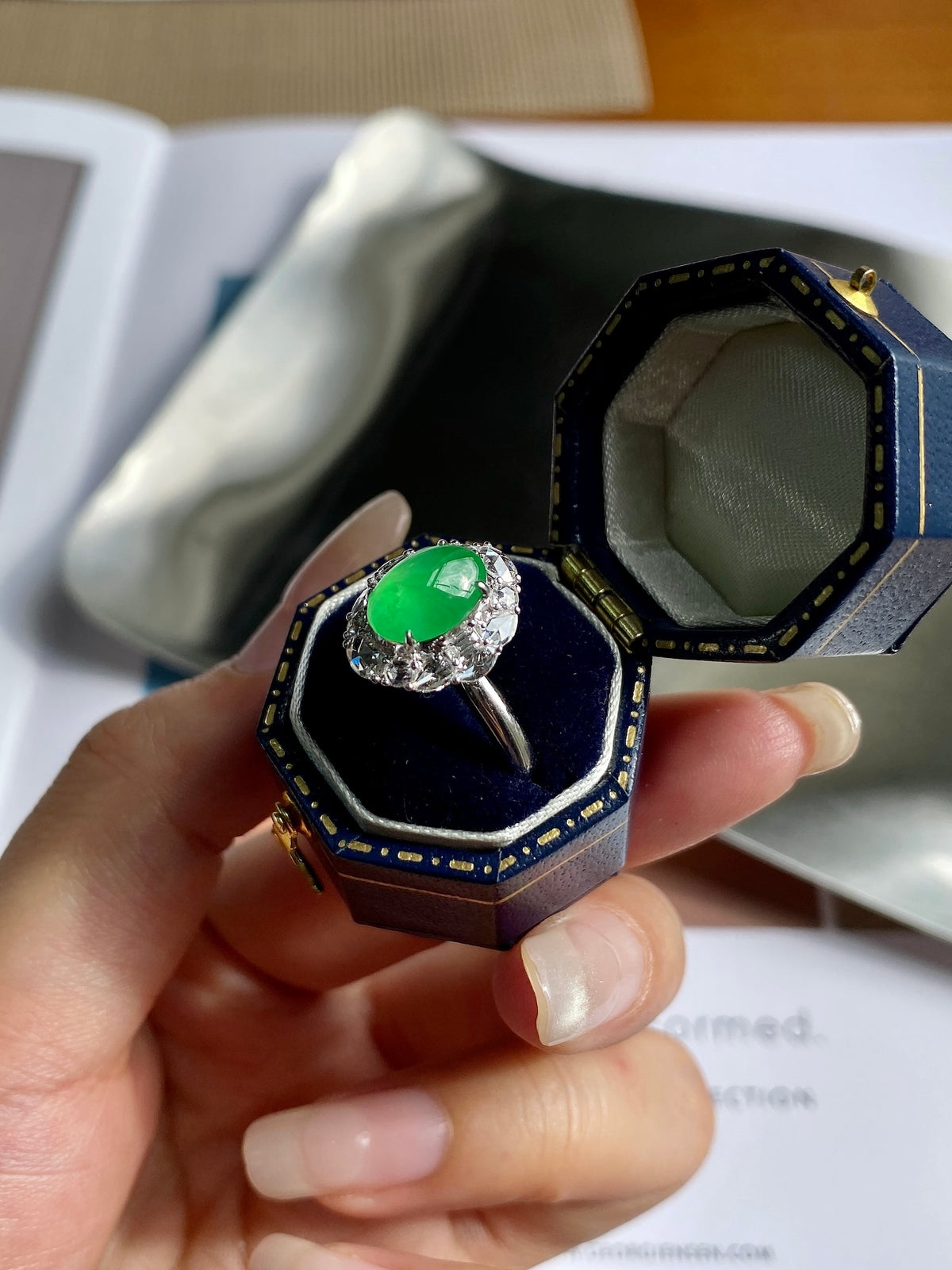 Green jade cabochon ring in blue presentation box with silver-tone halo setting