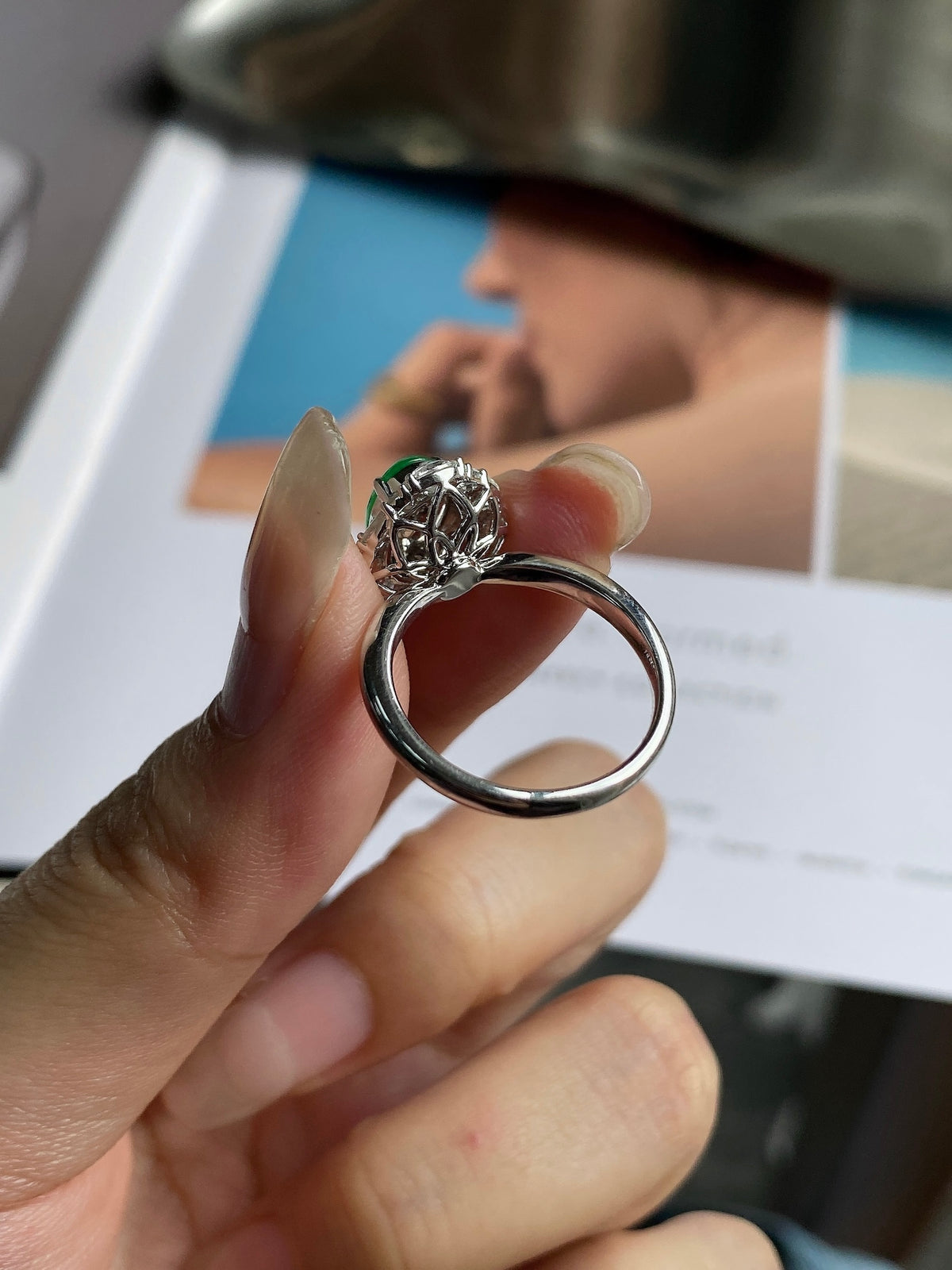 Green jade cabochon ring with silver-tone setting and round halo, held in hand