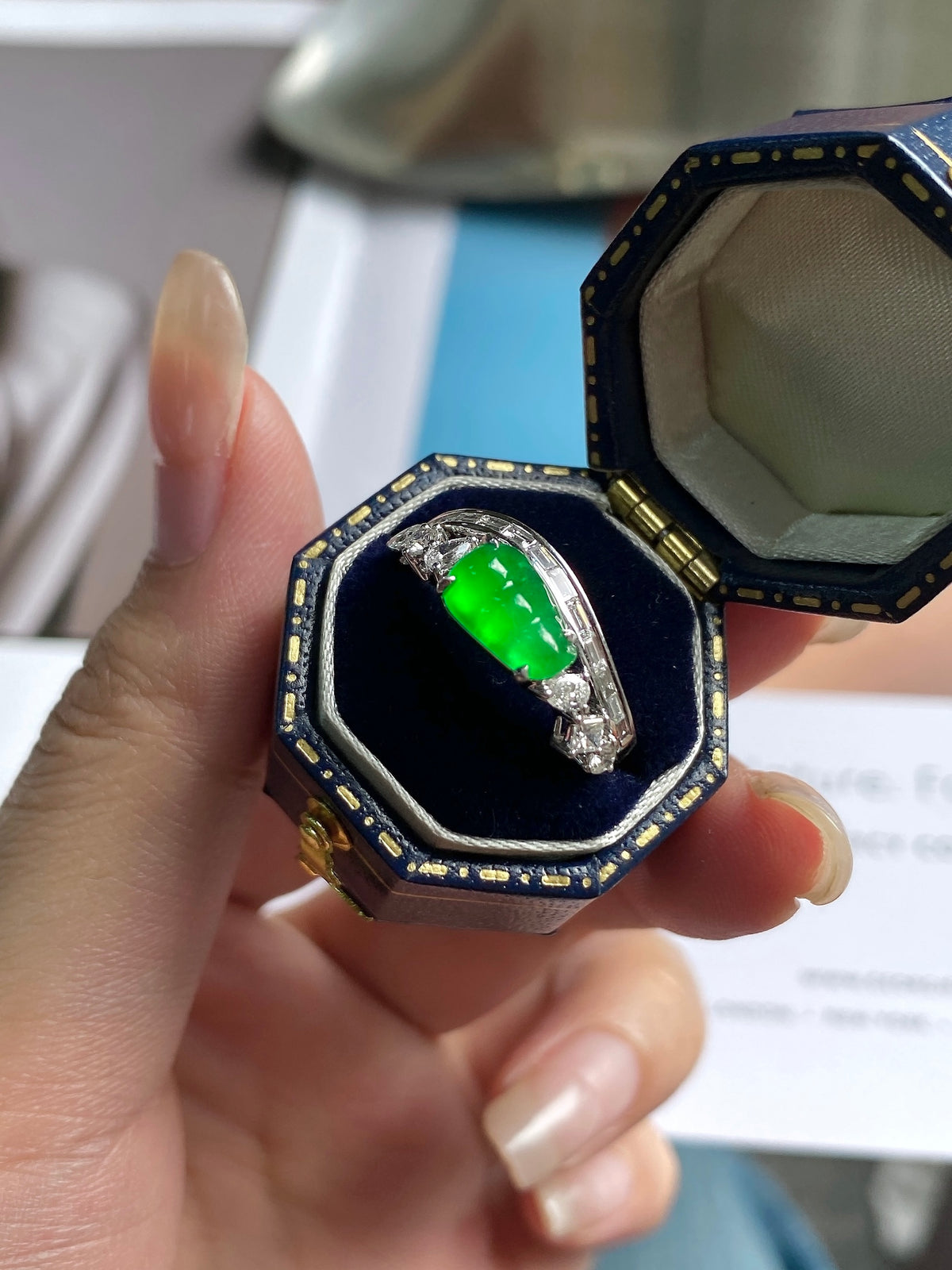 Green jadeite bean ring in open navy box, oval green center with clear accents