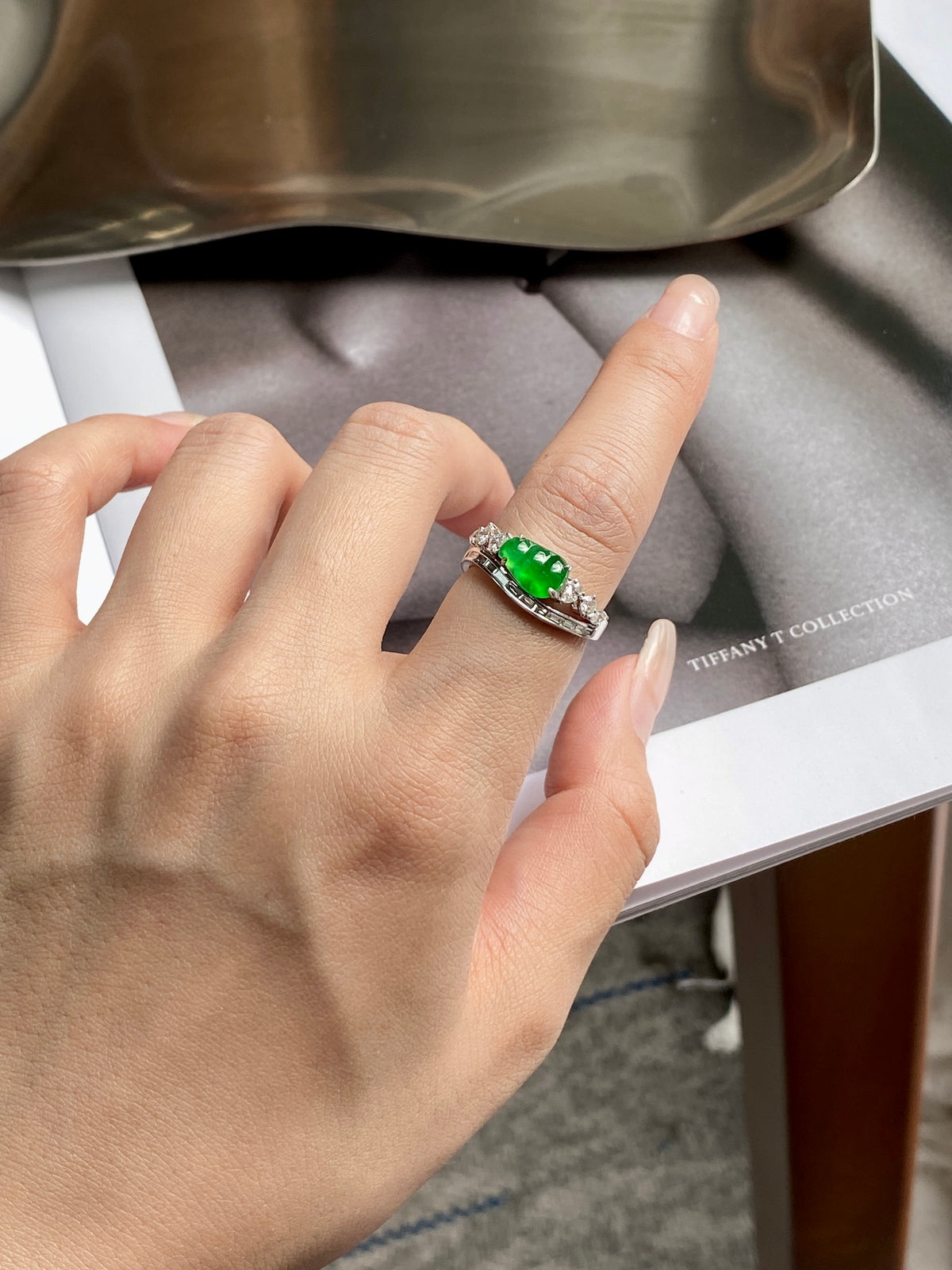 Green jadeite bean ring on finger, silver prong setting with clear side stones