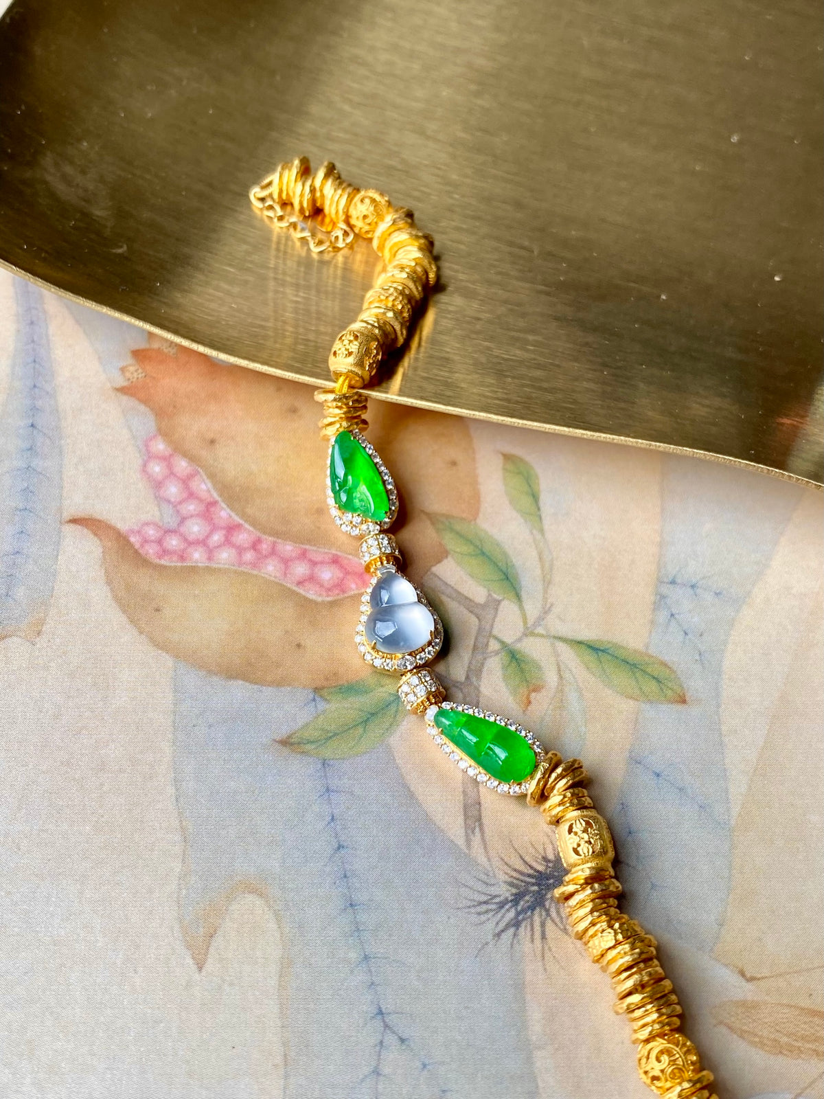 Gold jadeite gourd bracelet with green stones and blue pearl-like drop links