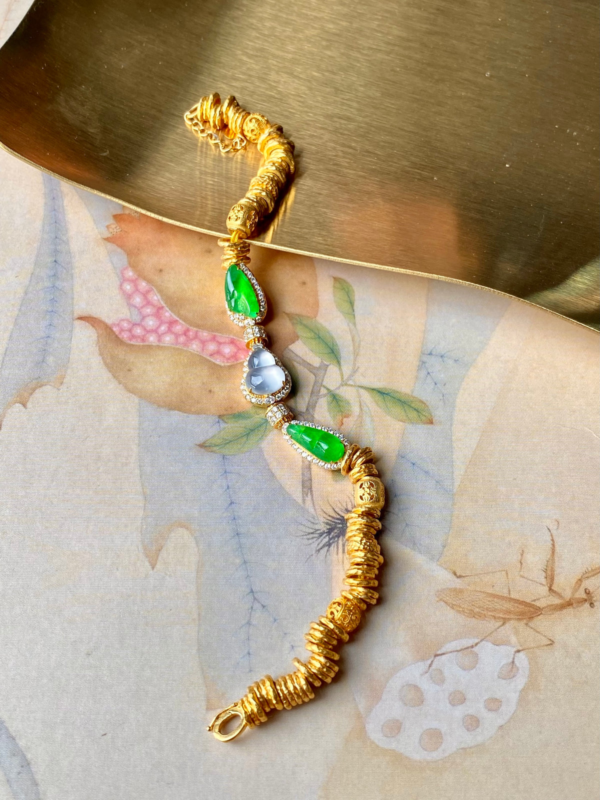 Gold jadeite gourd bracelet with green teardrops, blue center stone, clasp end