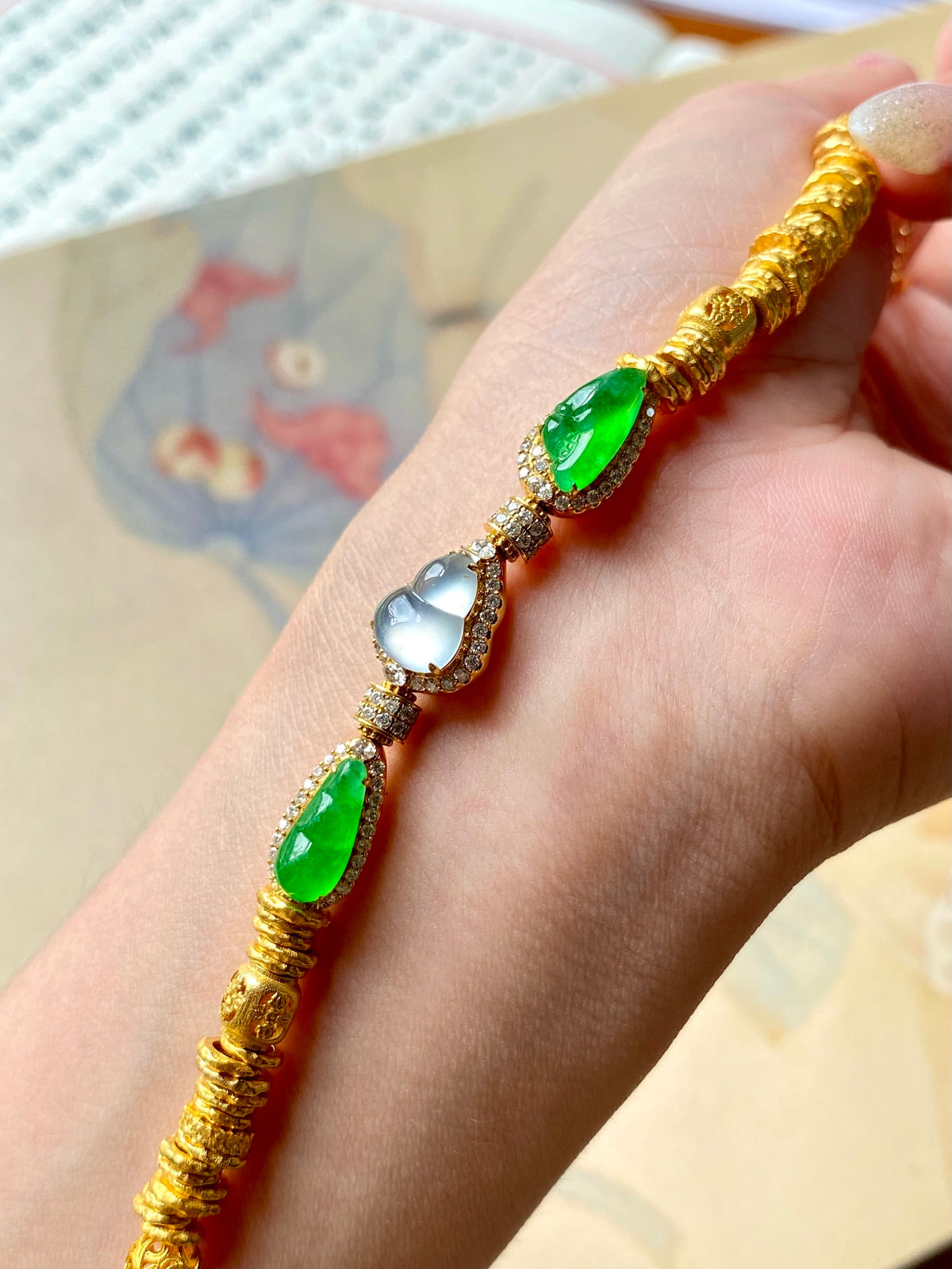 Gold jadeite gourd bracelet on hand with green teardrop stones and blue round gem