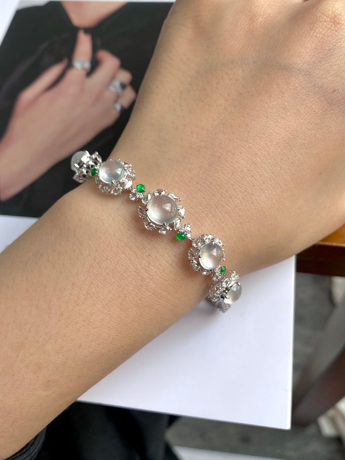 Cabochon bracelet on wrist with oval white center stones and green accent prongs