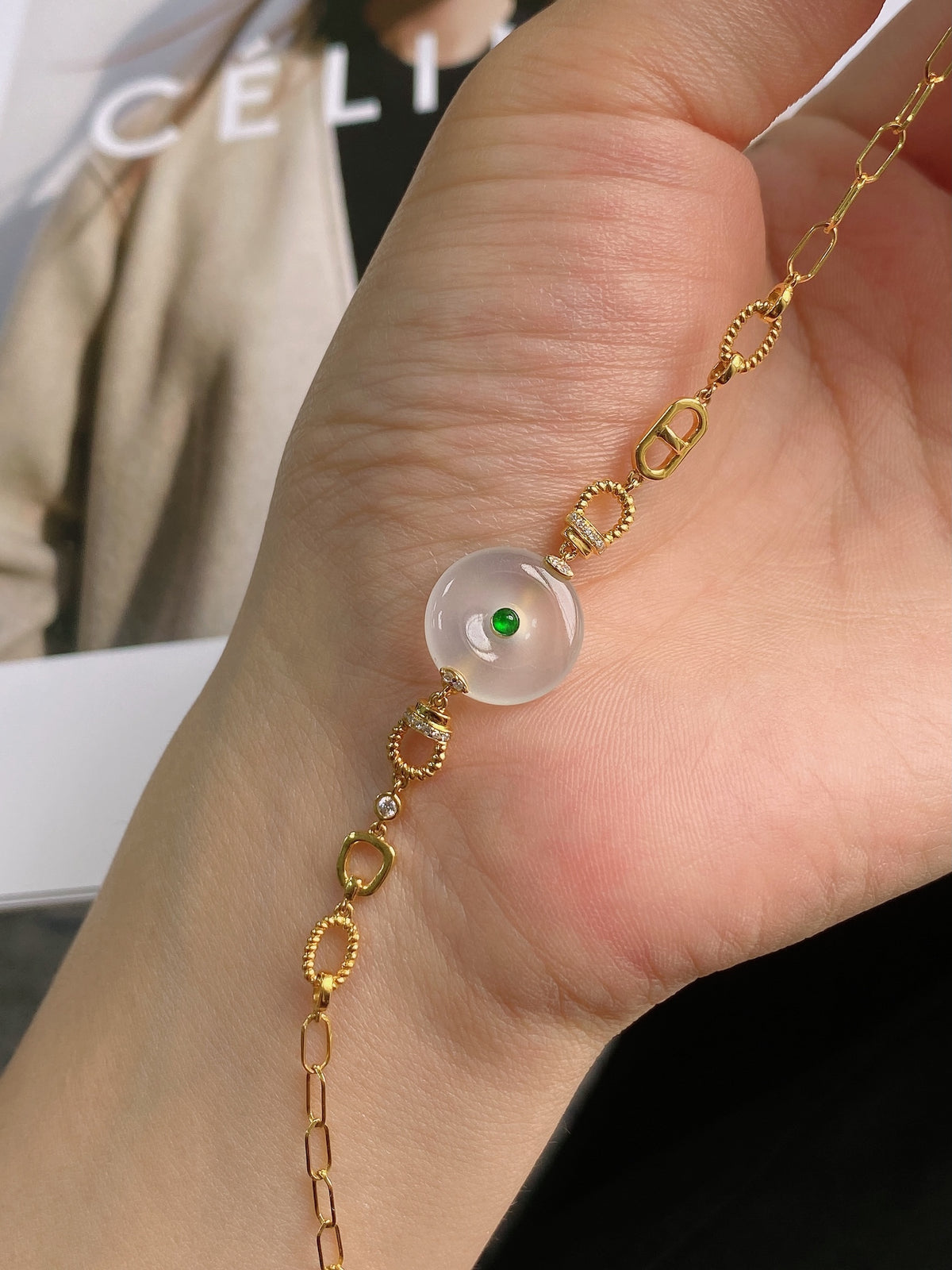 Gold bracelet with white jade disc bead, green center, and link chain on hand