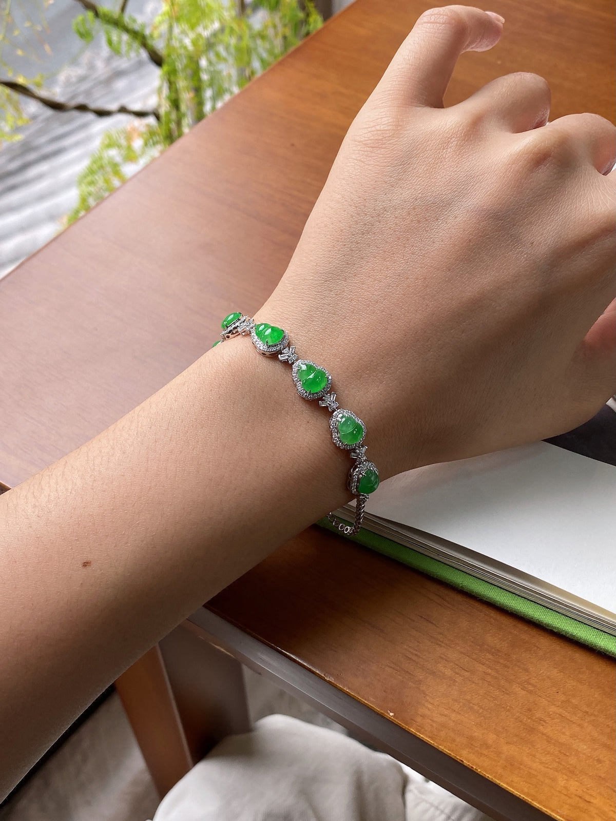 Green jadeite cabochon bracelet worn on wrist with silver-toned link chain