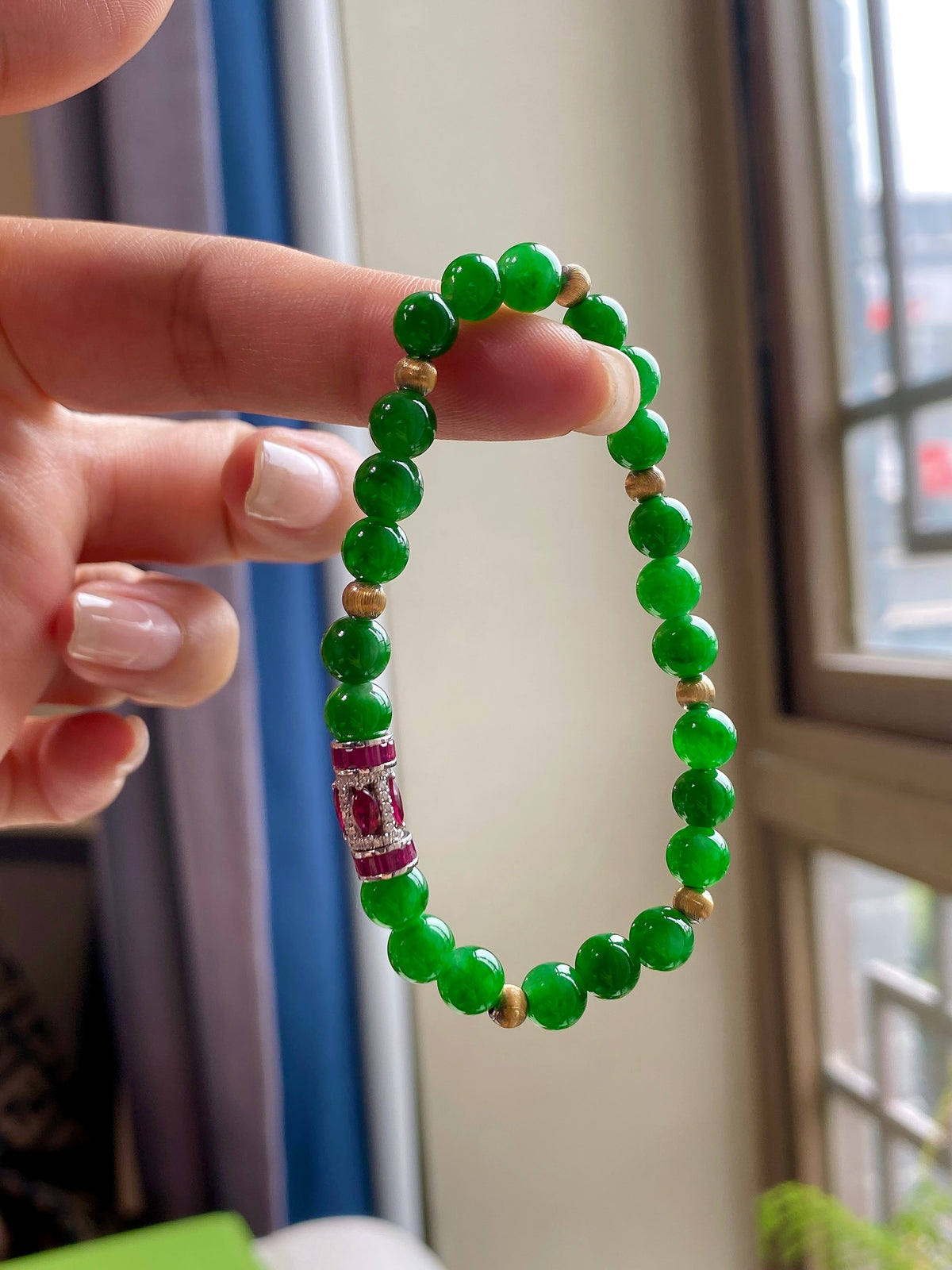 Green jadeite beaded bracelet held up; red centerpiece with gold spacers