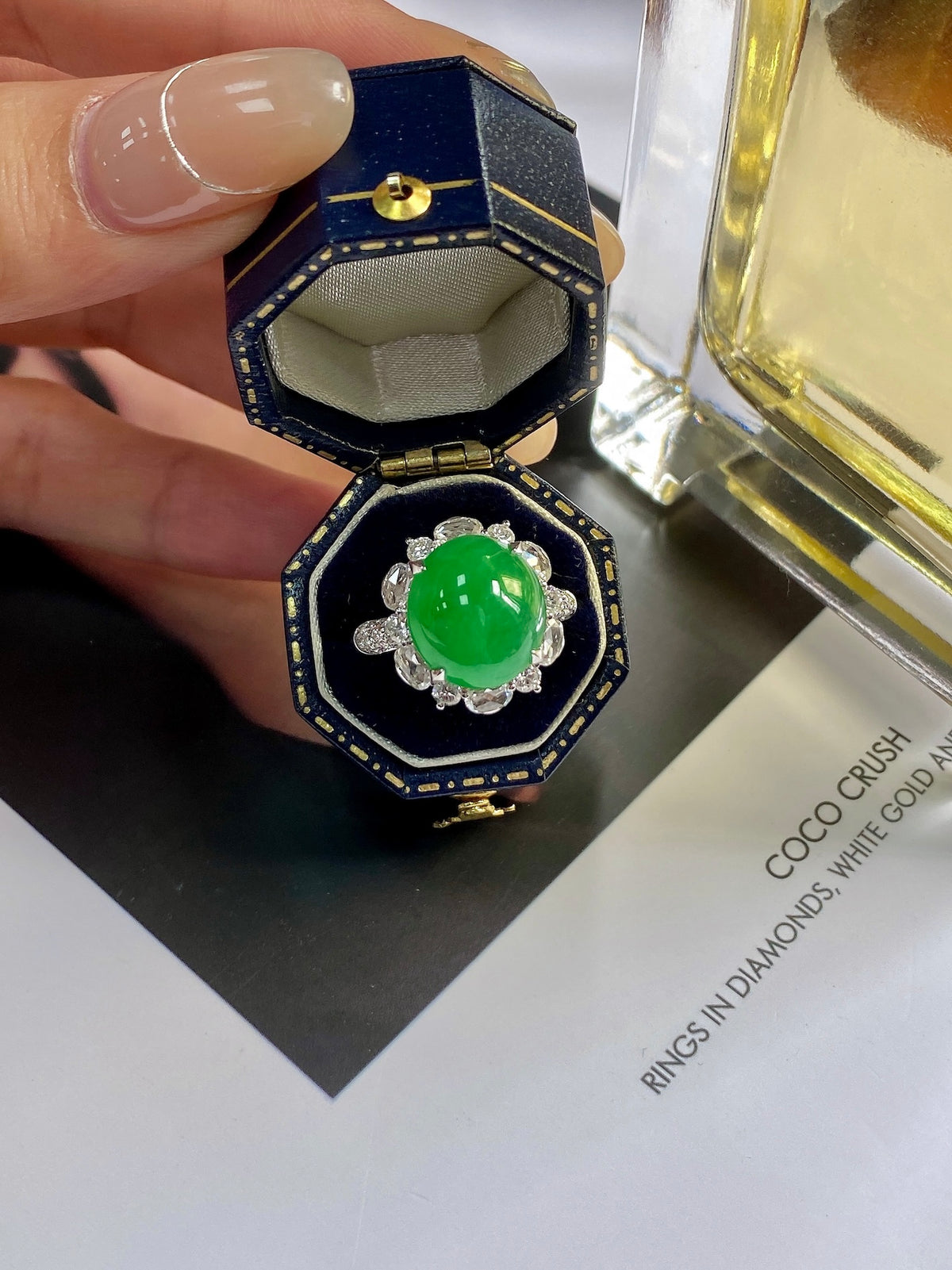 Green jadeite cabochon ring with silver halo, shown in octagon display box.