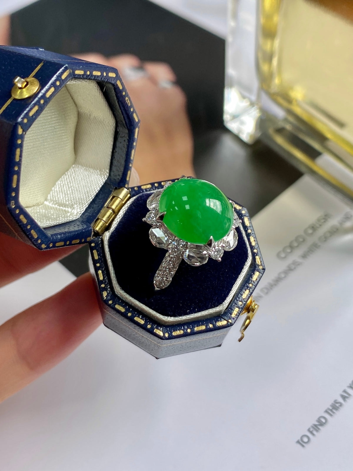 Green jadeite cabochon ring in open blue jewelry box with silver prongs halo.