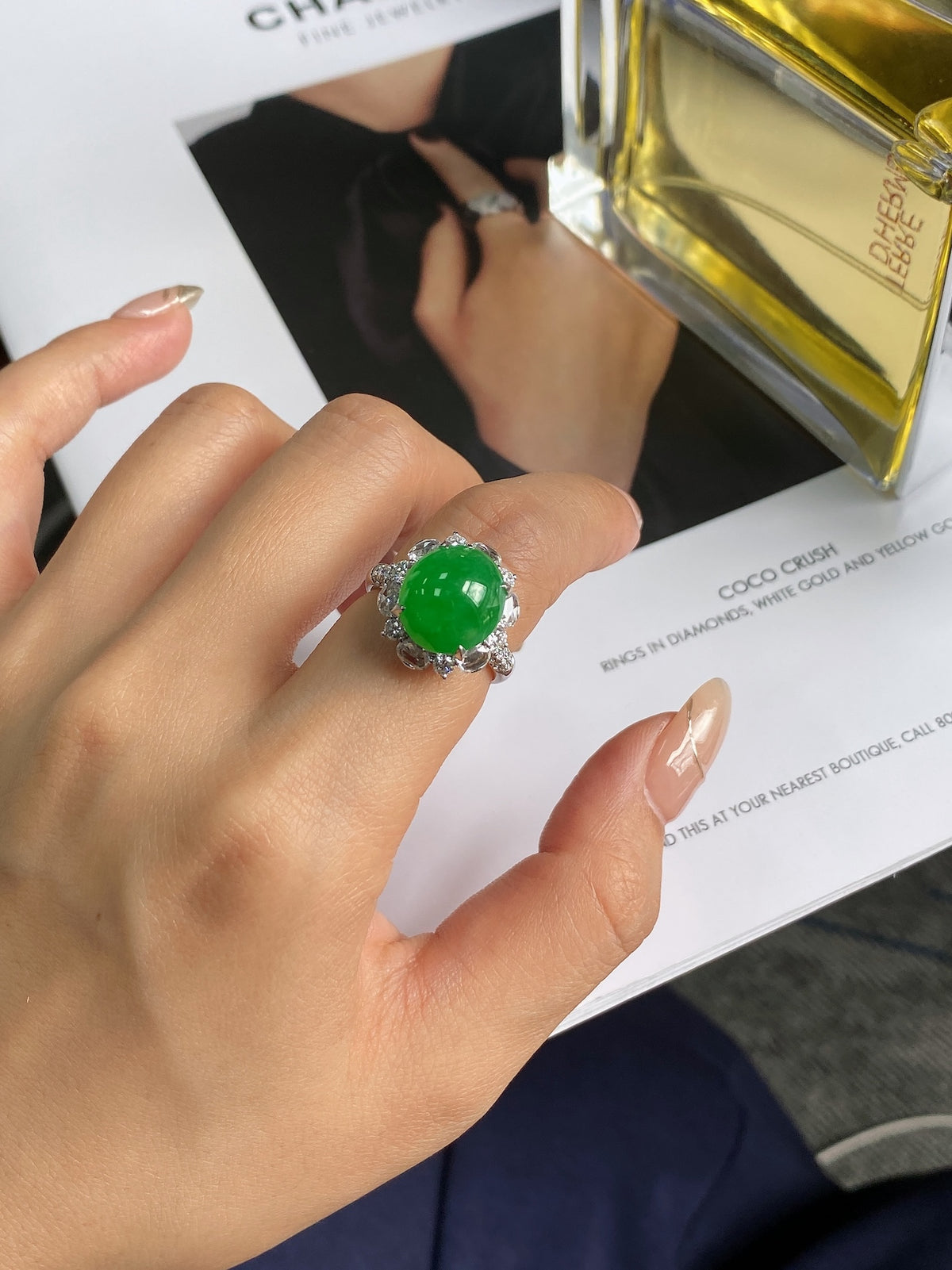 Green jadeite cabochon ring on finger with silver-tone prongs and halo.