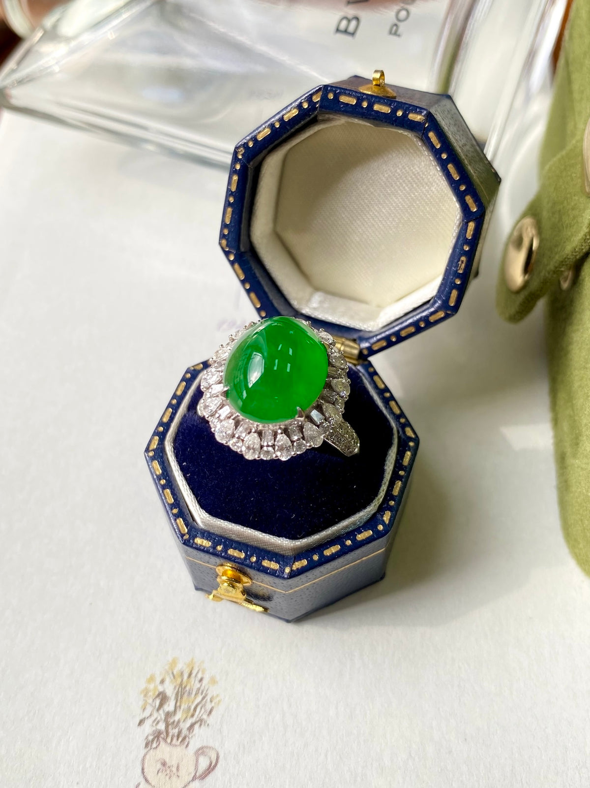 Green jadeite cabochon ring with diamond halo, displayed in an open box