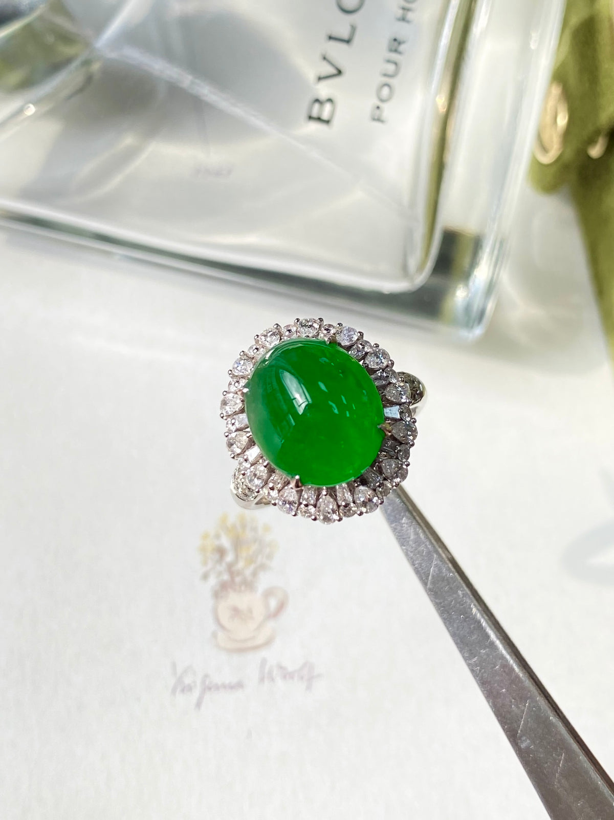 Oval green jadeite cabochon ring with diamond halo, held with tweezers