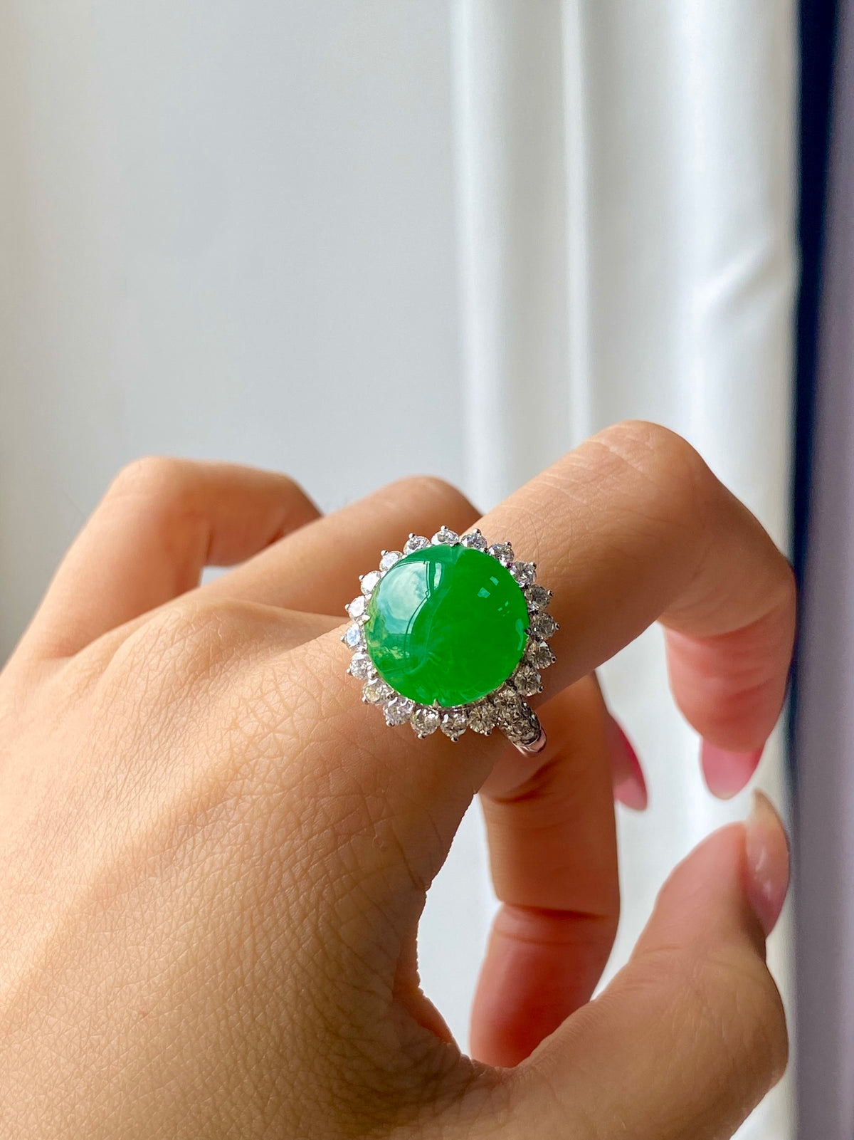 Green jadeite cabochon ring with diamond halo on finger, angled view