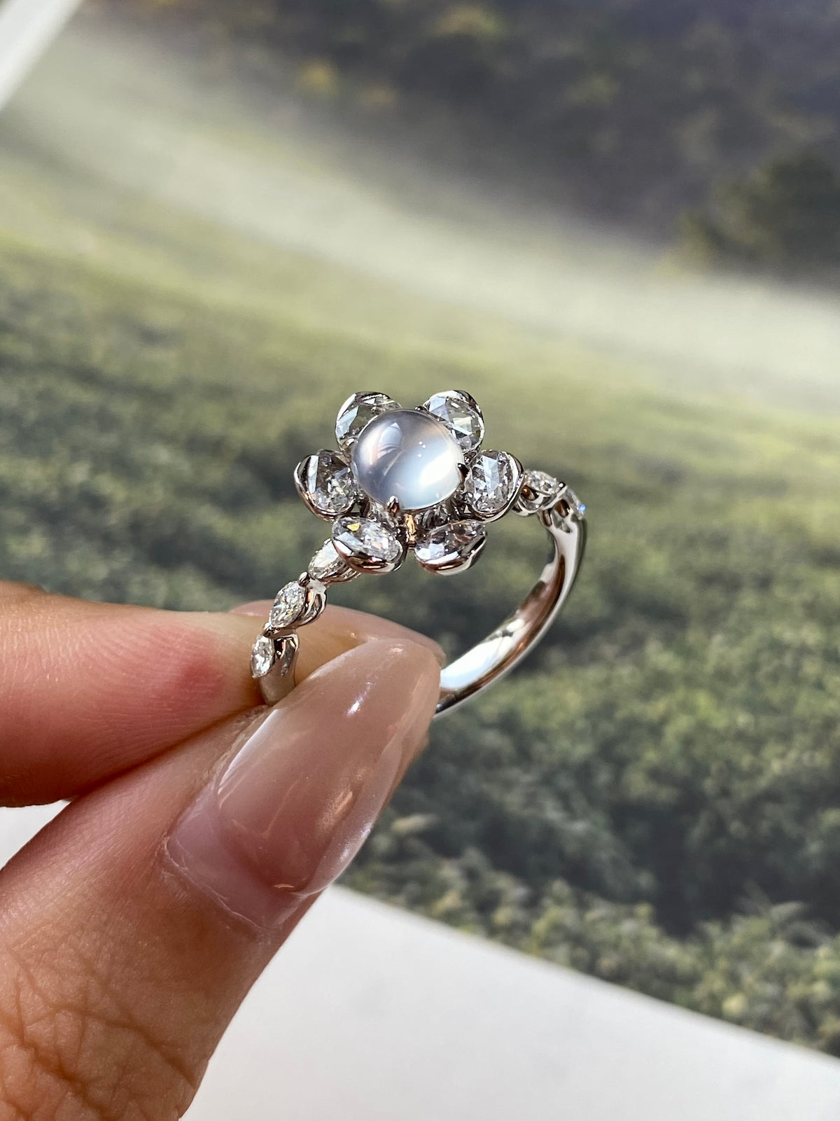 Light gray-white cabochon ring with multi-stone halo and delicate crystal side details