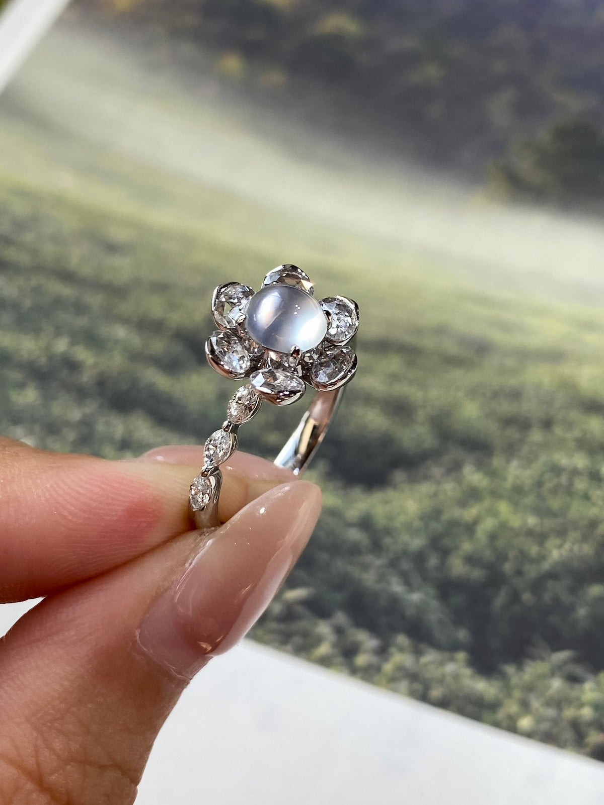 Round light gray-white cabochon ring with clustered crystal halo and curved metal band