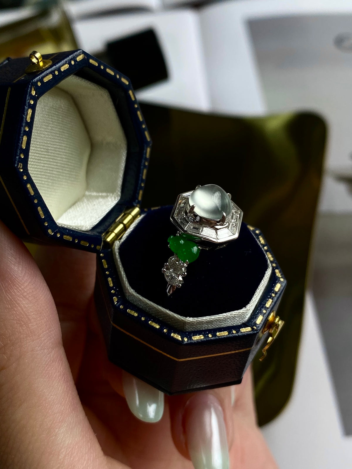 Cabochon ring with pale stone and green drops, in open blue-lined presentation box