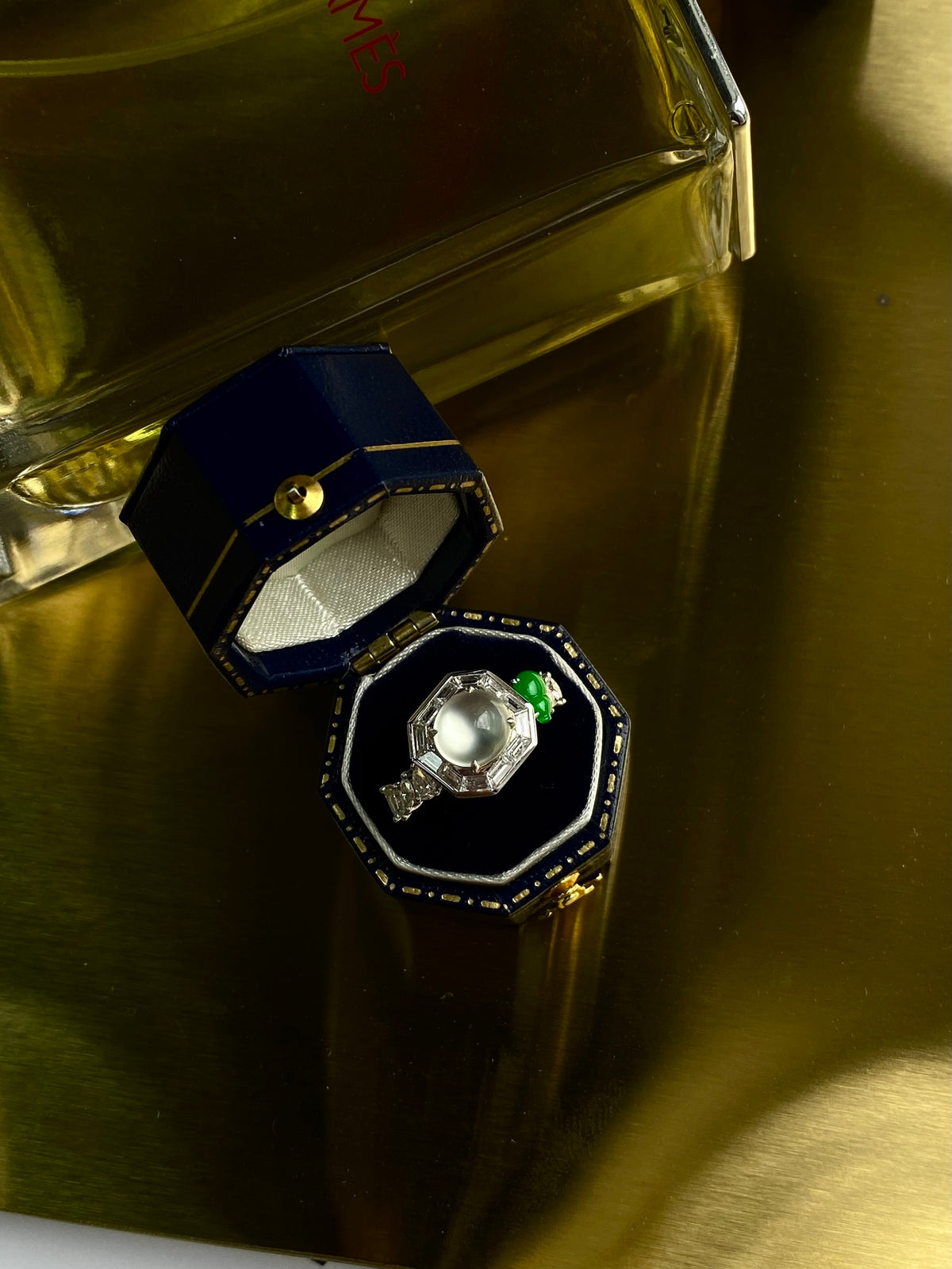 Cabochon ring with pale center stone and green accent, in blue presentation case