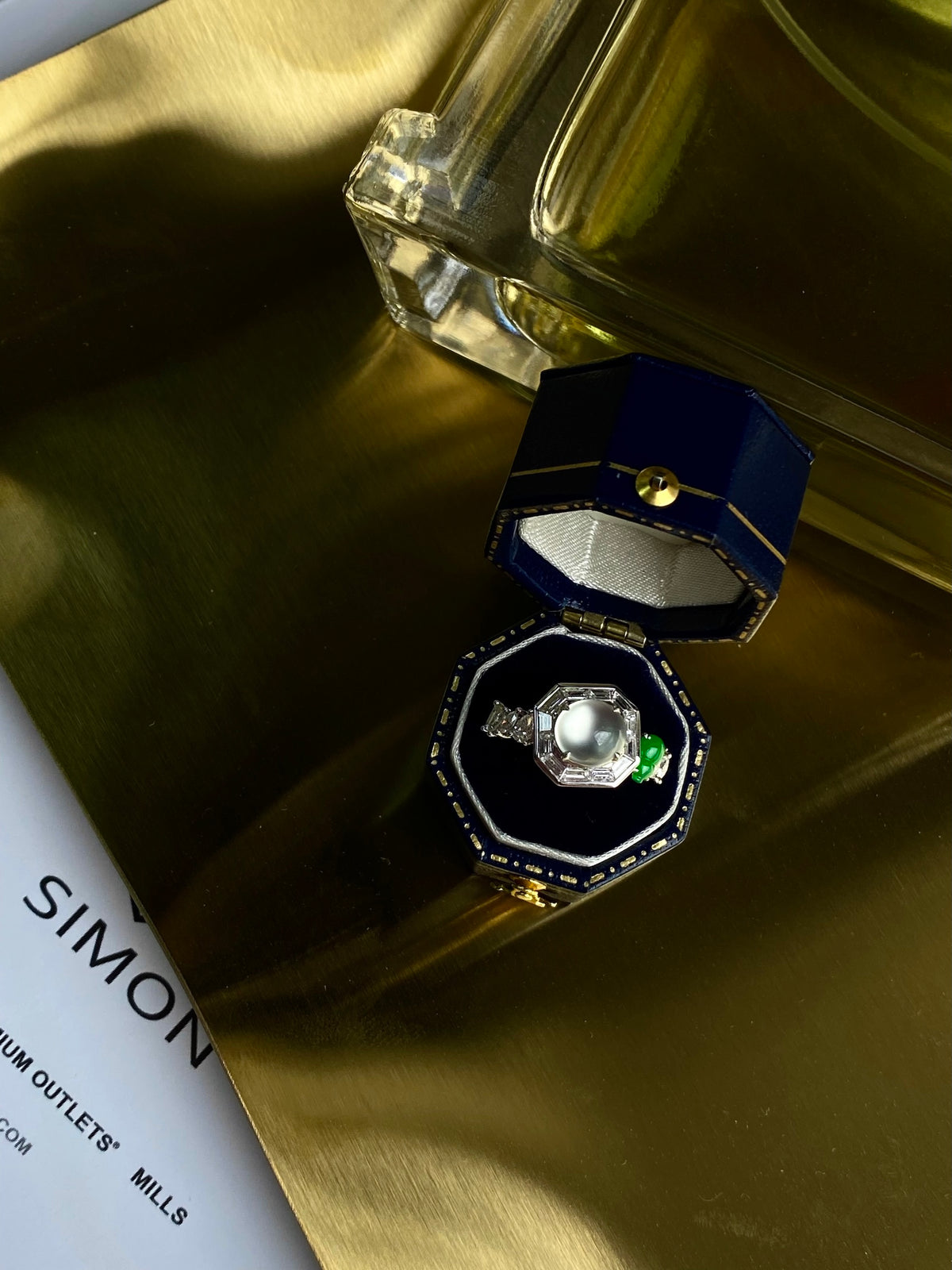 Cabochon ring with pale stone and green accent, resting in blue-lined box