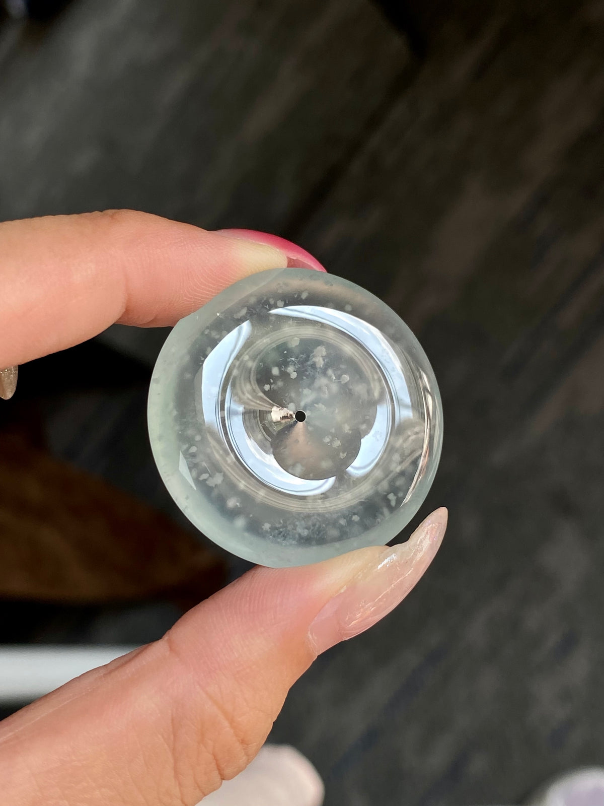 Round jadeite safety disc with clear metal ring, speckled inclusions, central pin.