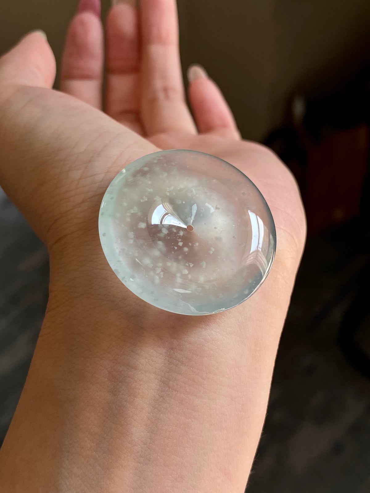 Round jadeite safety disc with frosted speckled inclusions and central pin on palm.