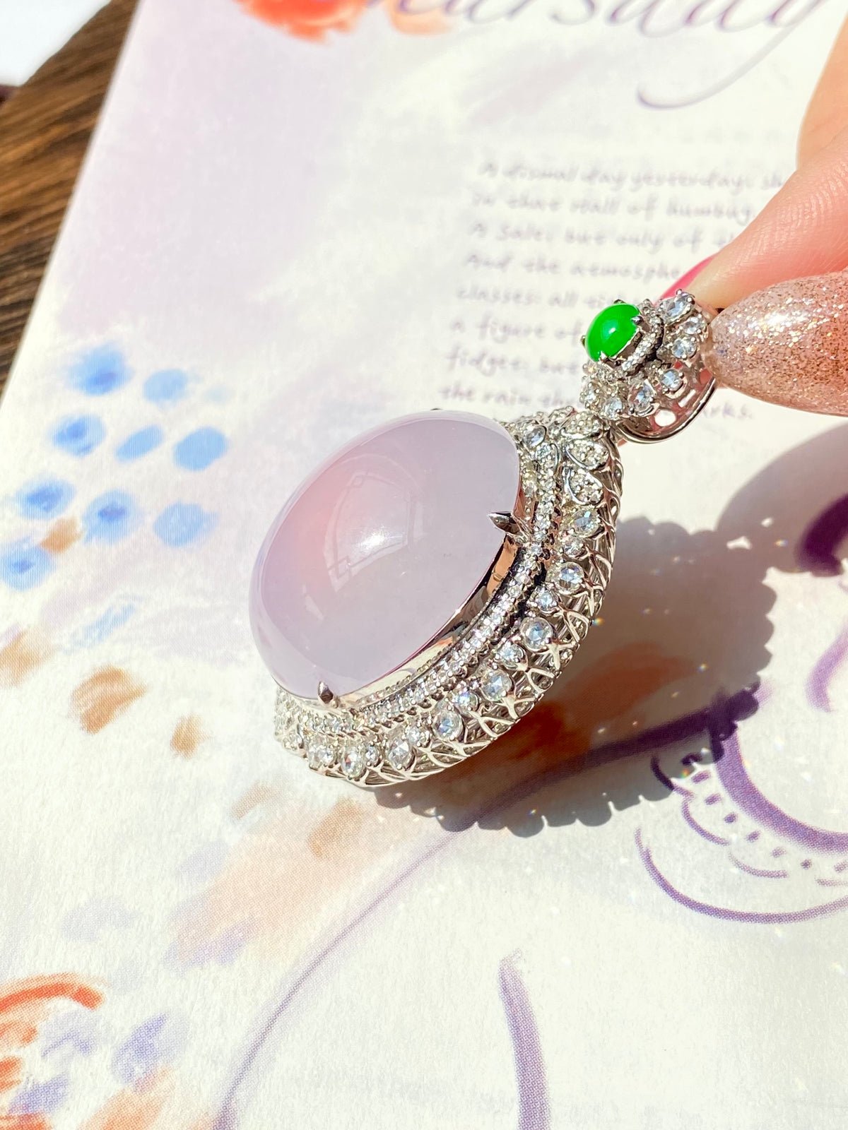 Lavender oval cabochon pendant with green round accent and jeweled halo on black cord