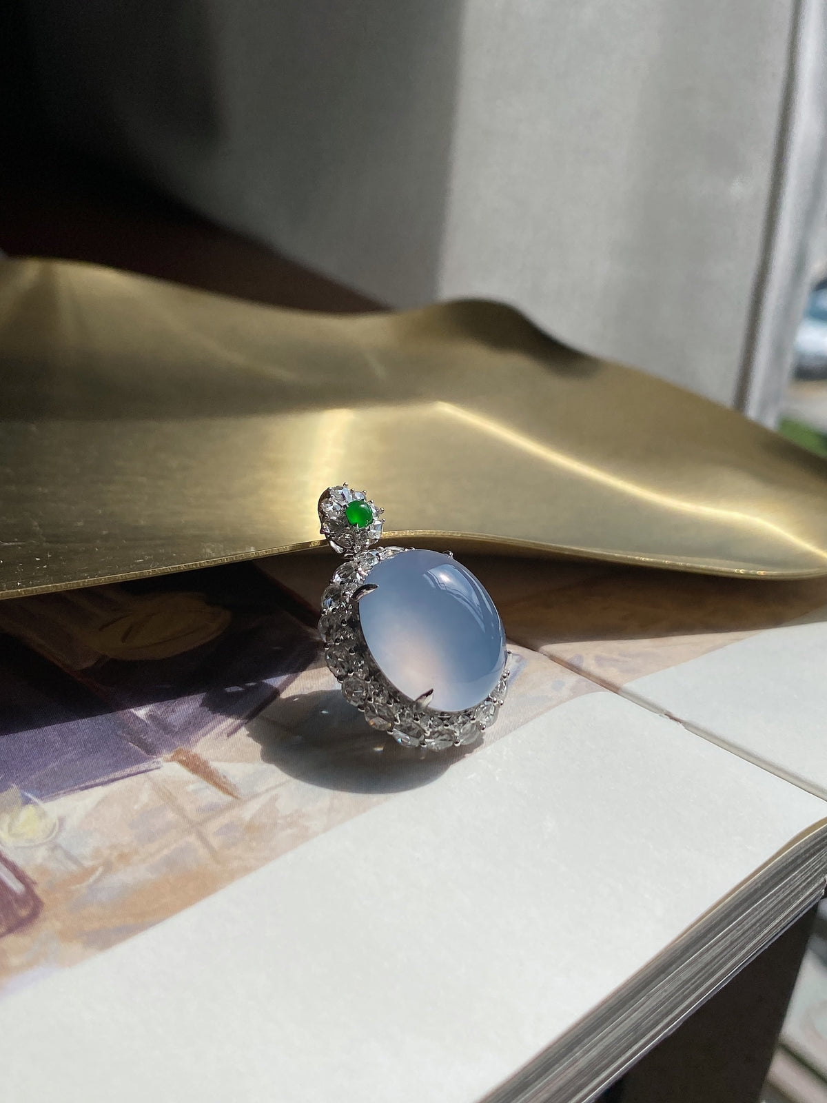Oval light blue cabochon pendant with crystal halo and green accent stone