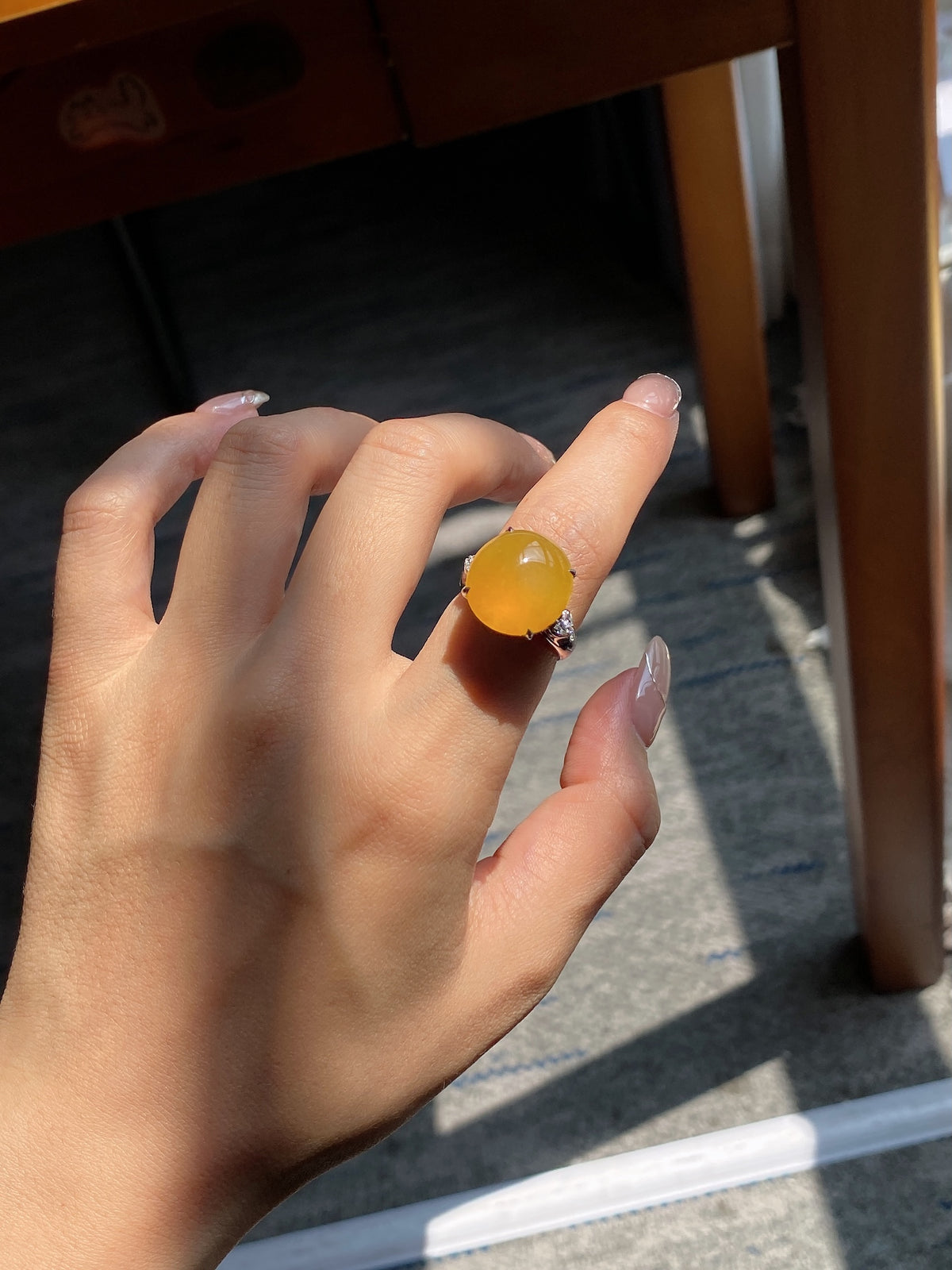 Jadeite cabochon ring on hand featuring golden yellow oval stone in dark blue frame