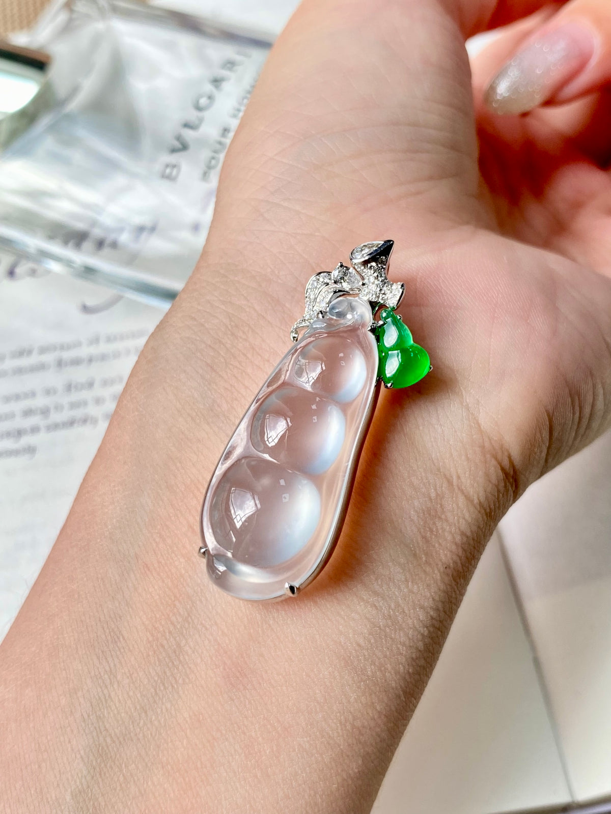 Jadeite bean pendant on hand: clear teardrop stone with diamond-like setting and green charm