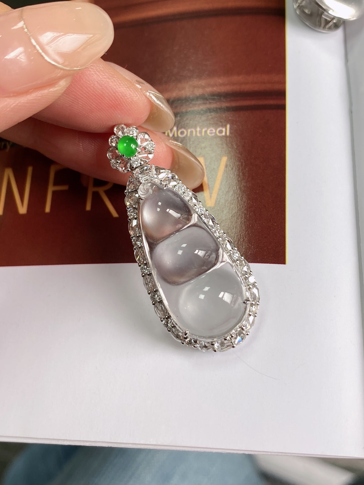 Silver bean pendant with green cabochon and three oval white stones, close-up