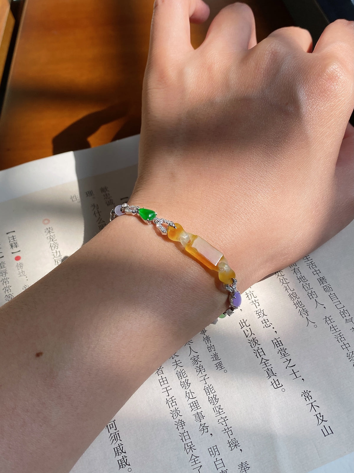 Yellow jadeite bead bracelet on wrist with silver chain and green-orange gemstone beads