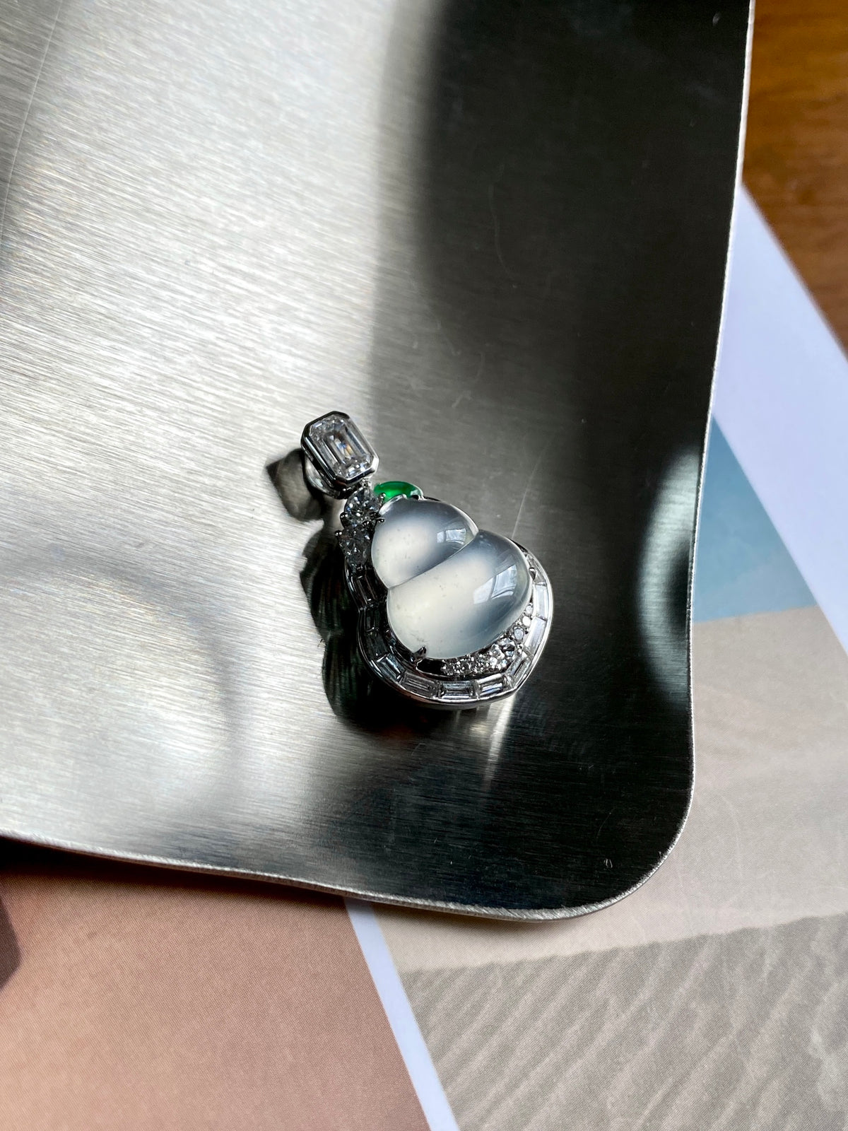 Silver gourd pendant with oval light green center stone, close-up on metallic card