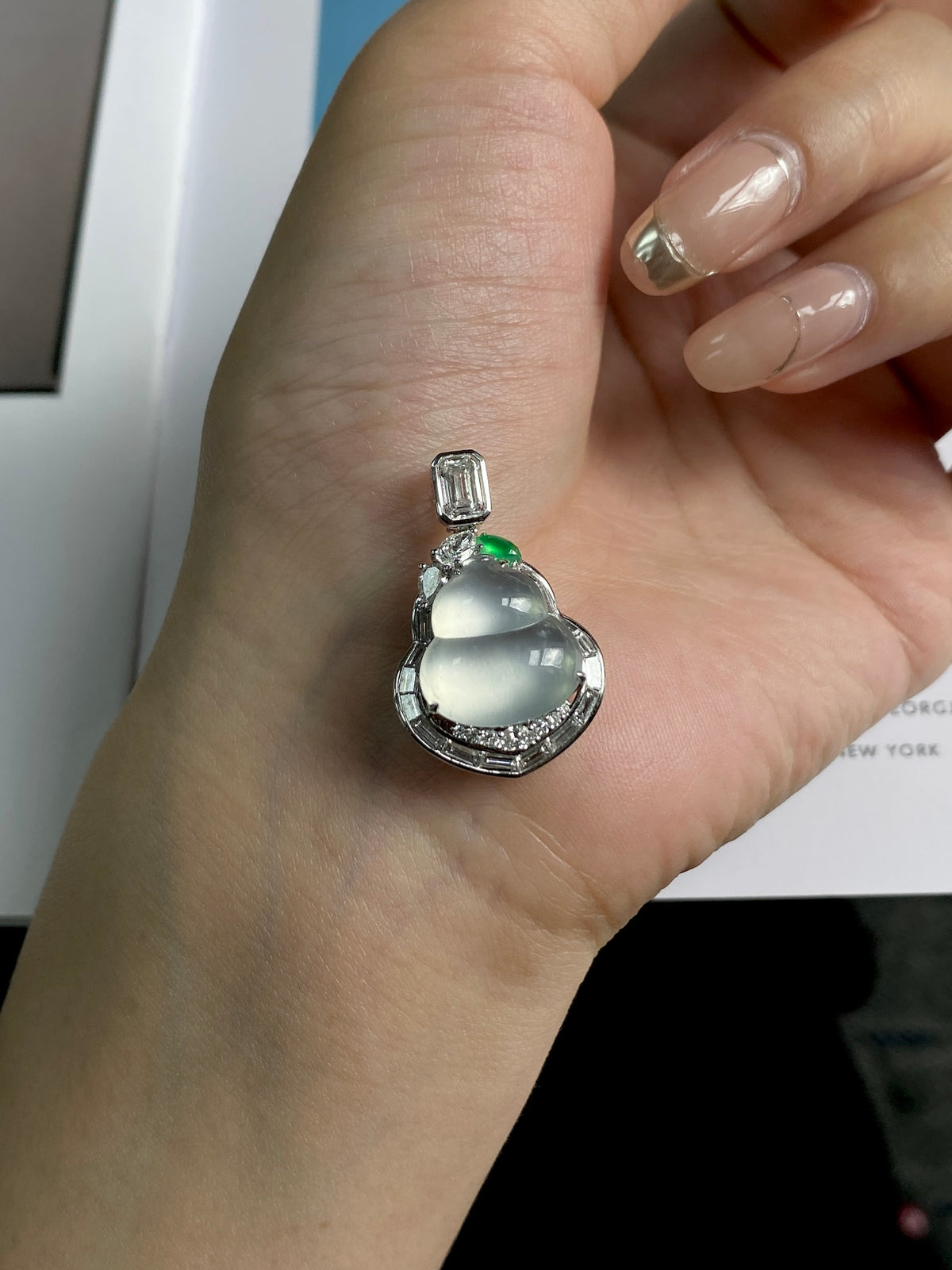 Silver pendant with oval light green stone and small green gem, shown on palm