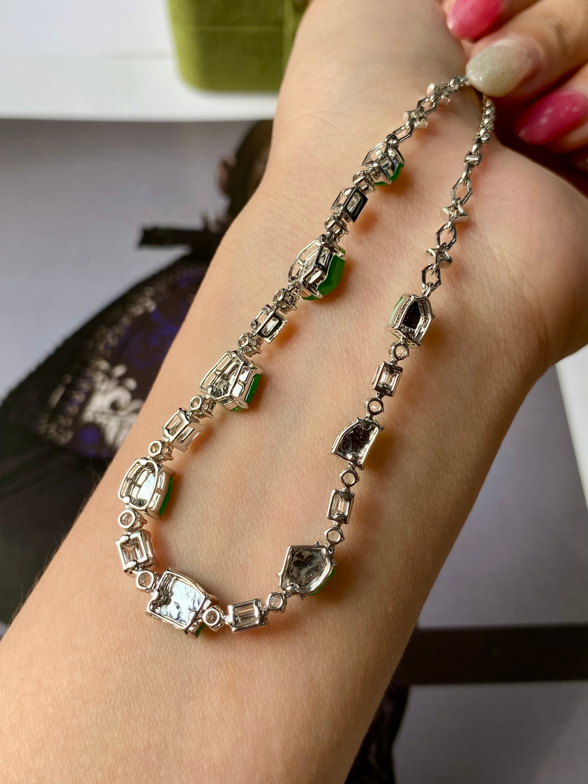 Green jadeite bead necklace on wrist with silver links and green gemstone stations