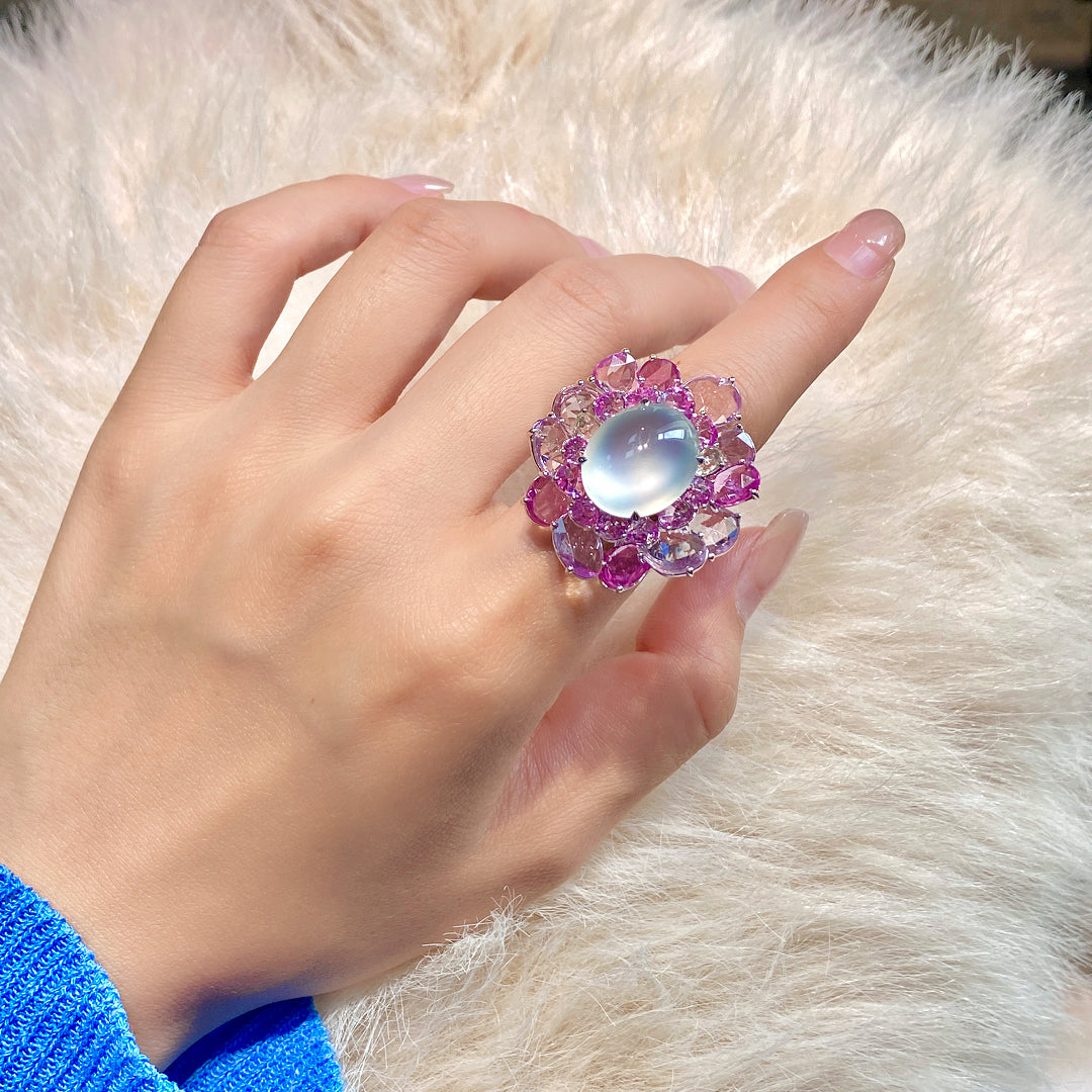 Floral gemstone ring with oval opalescent cabochon and purple halo, shown on hand