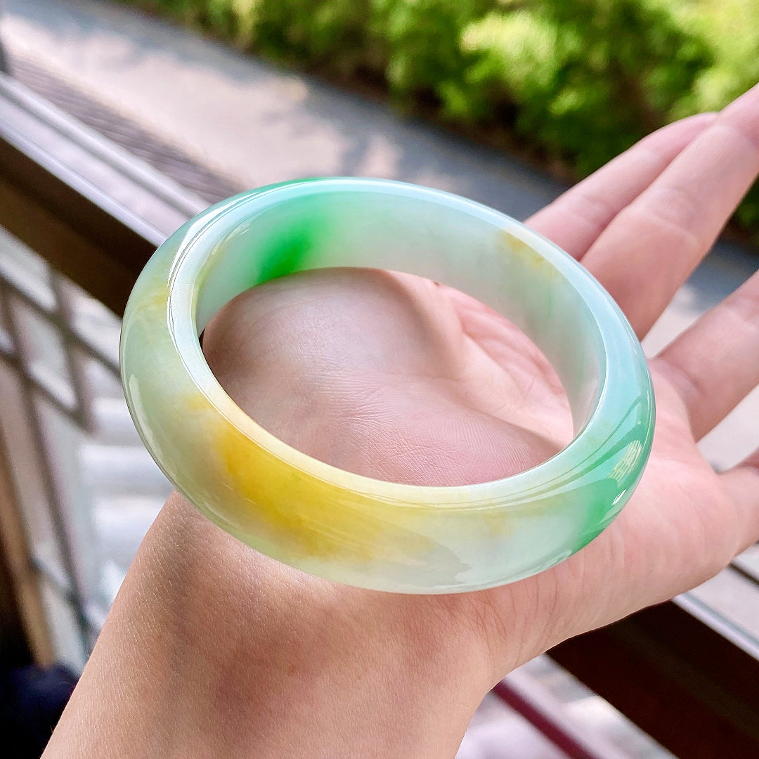 Jadeite bangle held in palm, translucent light green with yellow stripe and green spots