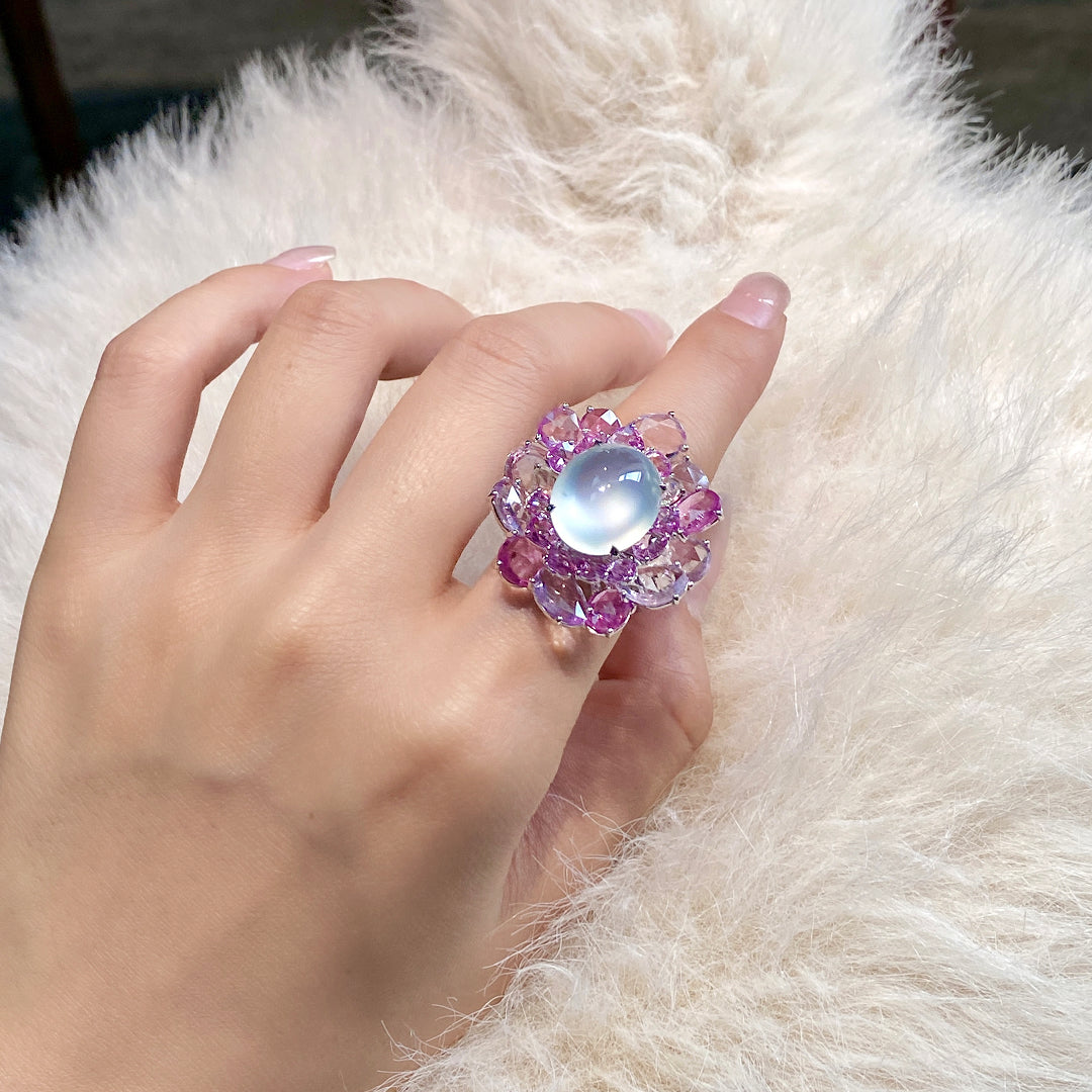 Floral gemstone ring with oval opalescent center and purple gemstone flowers on finger