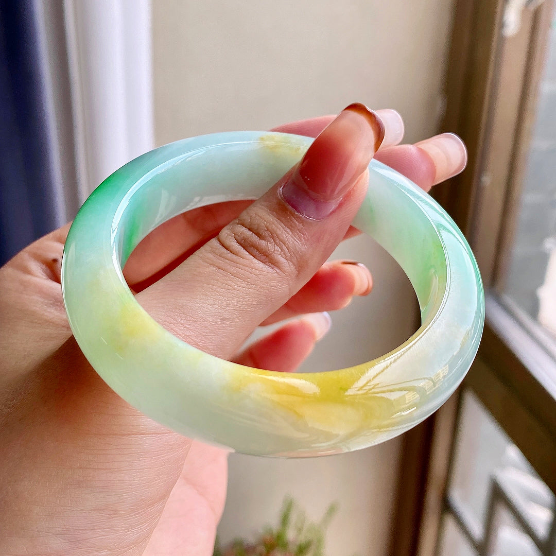 Jadeite bangle in hand, light green base with yellow and green swirls, round bracelet