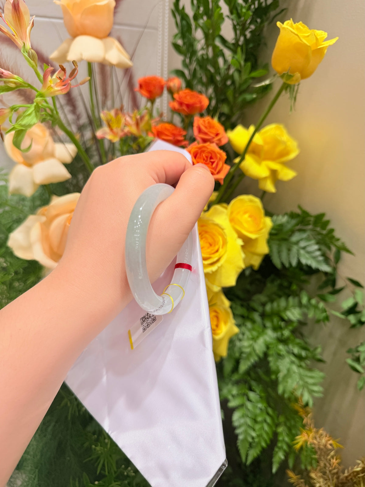 Misty-green round-bar jadeite bangle held near a white package bag