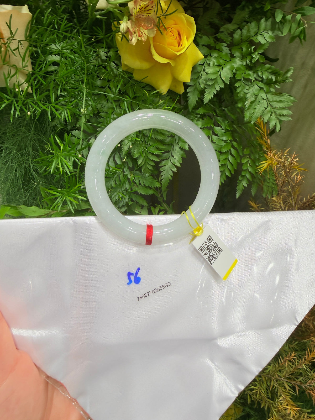 Misty-green round-bar jadeite bangle on white bag with barcode tag