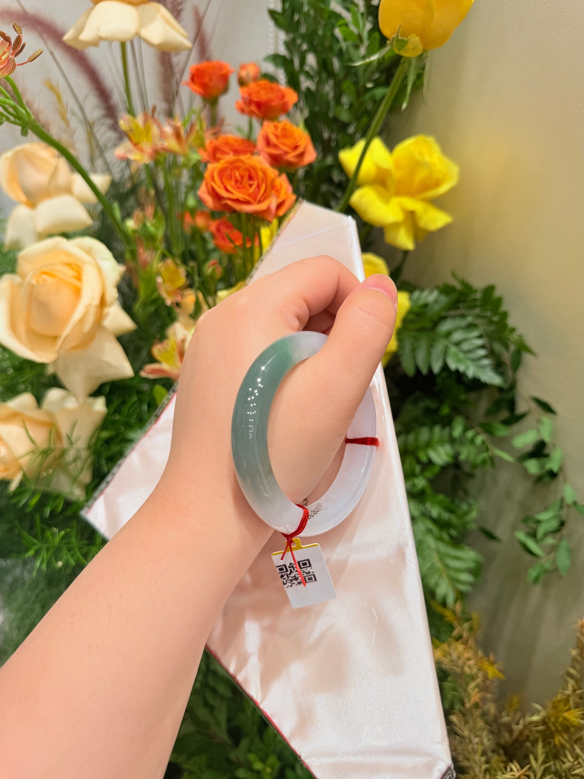 Light blue translucent jadeite-style bangle with red string tie on white wrap