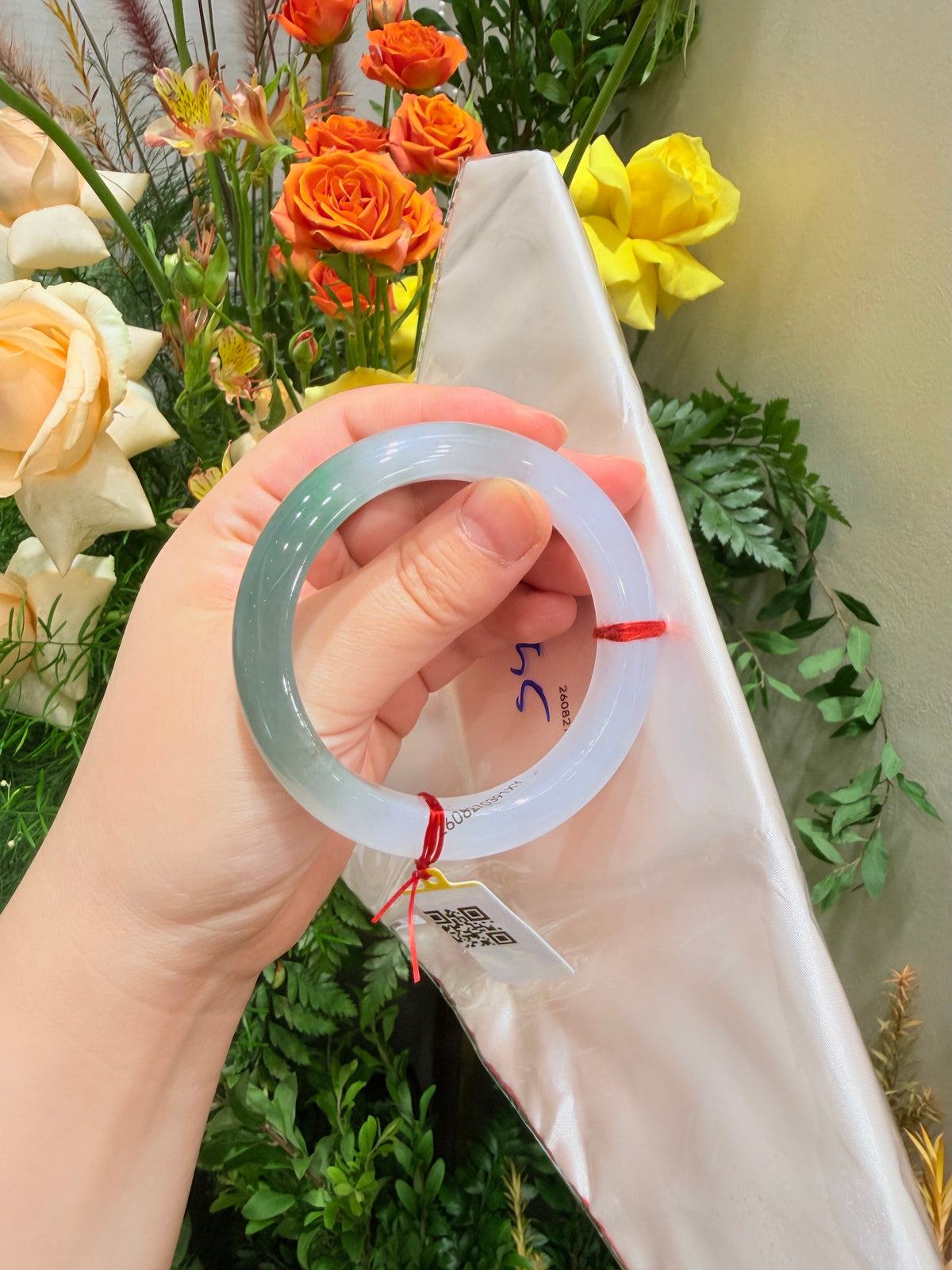 Light blue translucent bangle, close-up in hand, red string and tag visible
