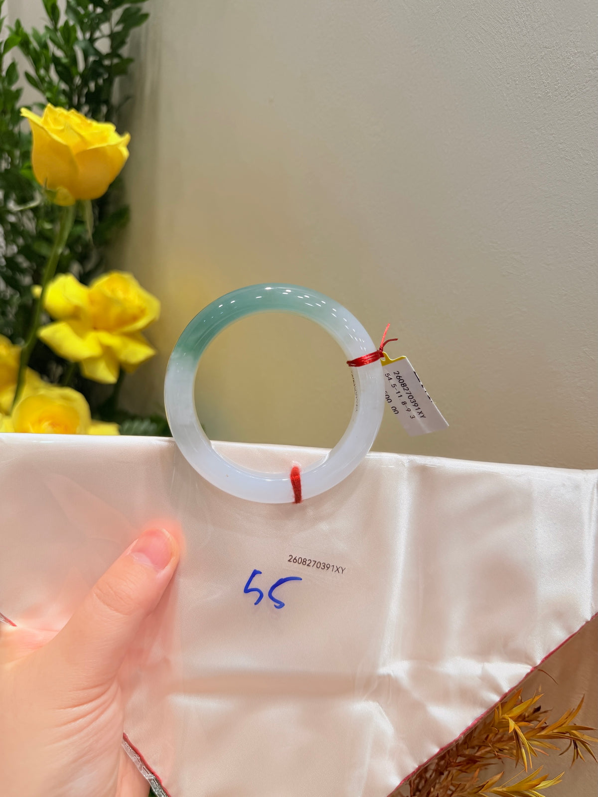 Light blue translucent bangle on white wrap, tag and small red string near opening