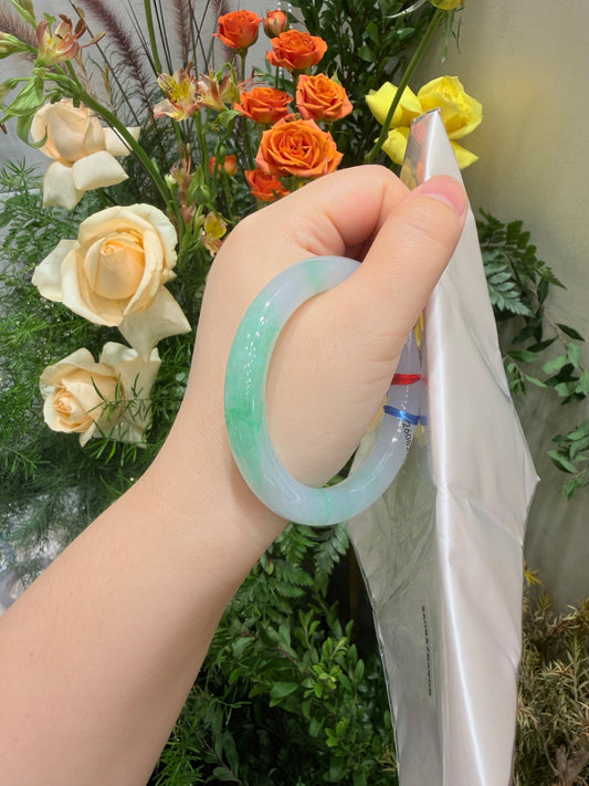 Pale mint-green jadeite bangle held in hand, smooth round bracelet with tag
